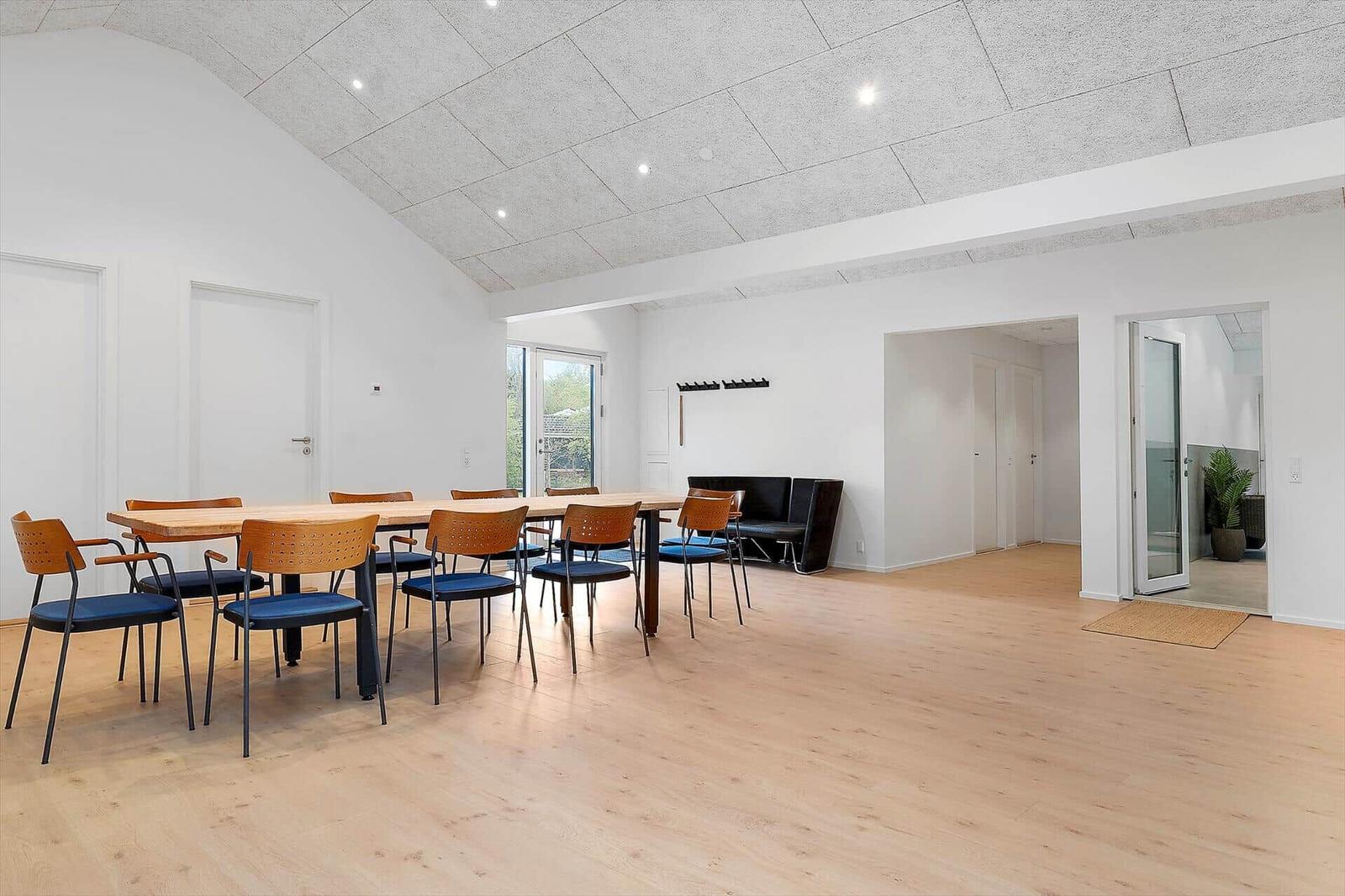 Großer Raum mit Holzboden, Tisch und Stühlen, Fenster und Türen.