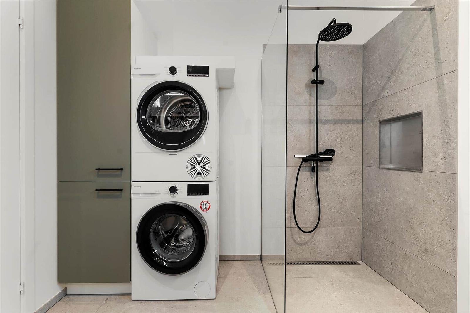 Waschmaschine und Trockner stehen neben Dusche mit Glaswand.