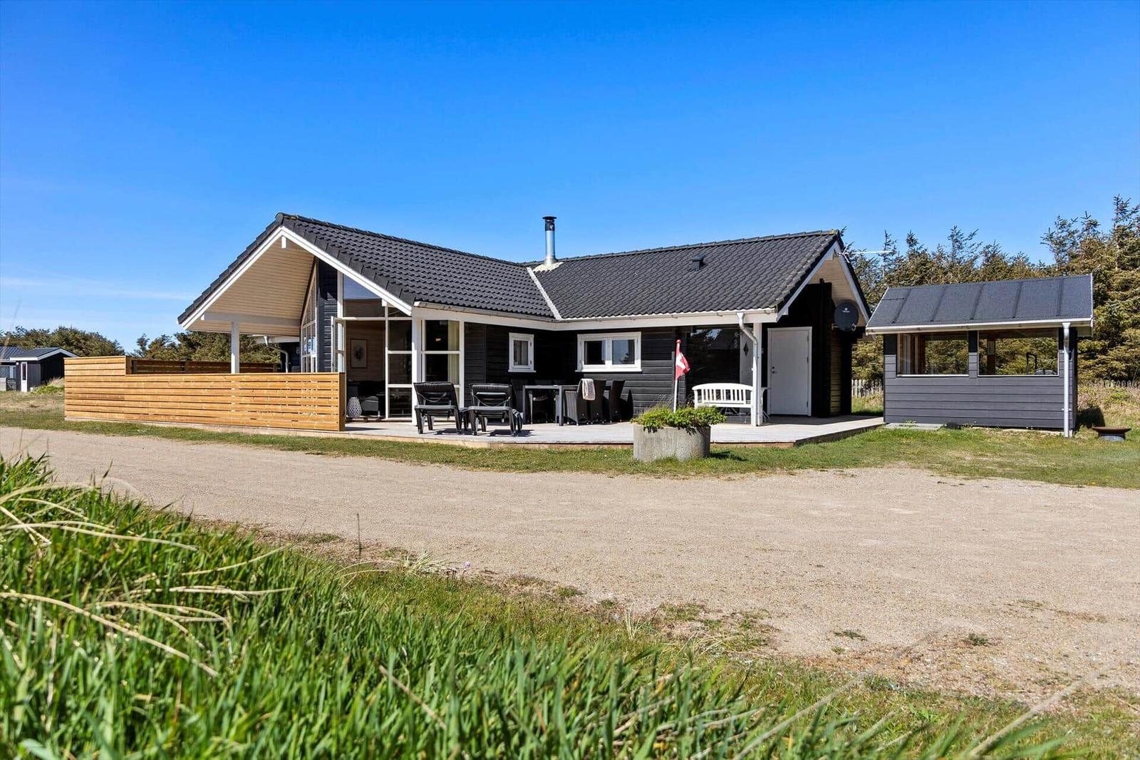 Moderne Ferienhaus mit Terrasse und Garten. Schwarze Fassade, Holzverkleidung und Grillbereich.