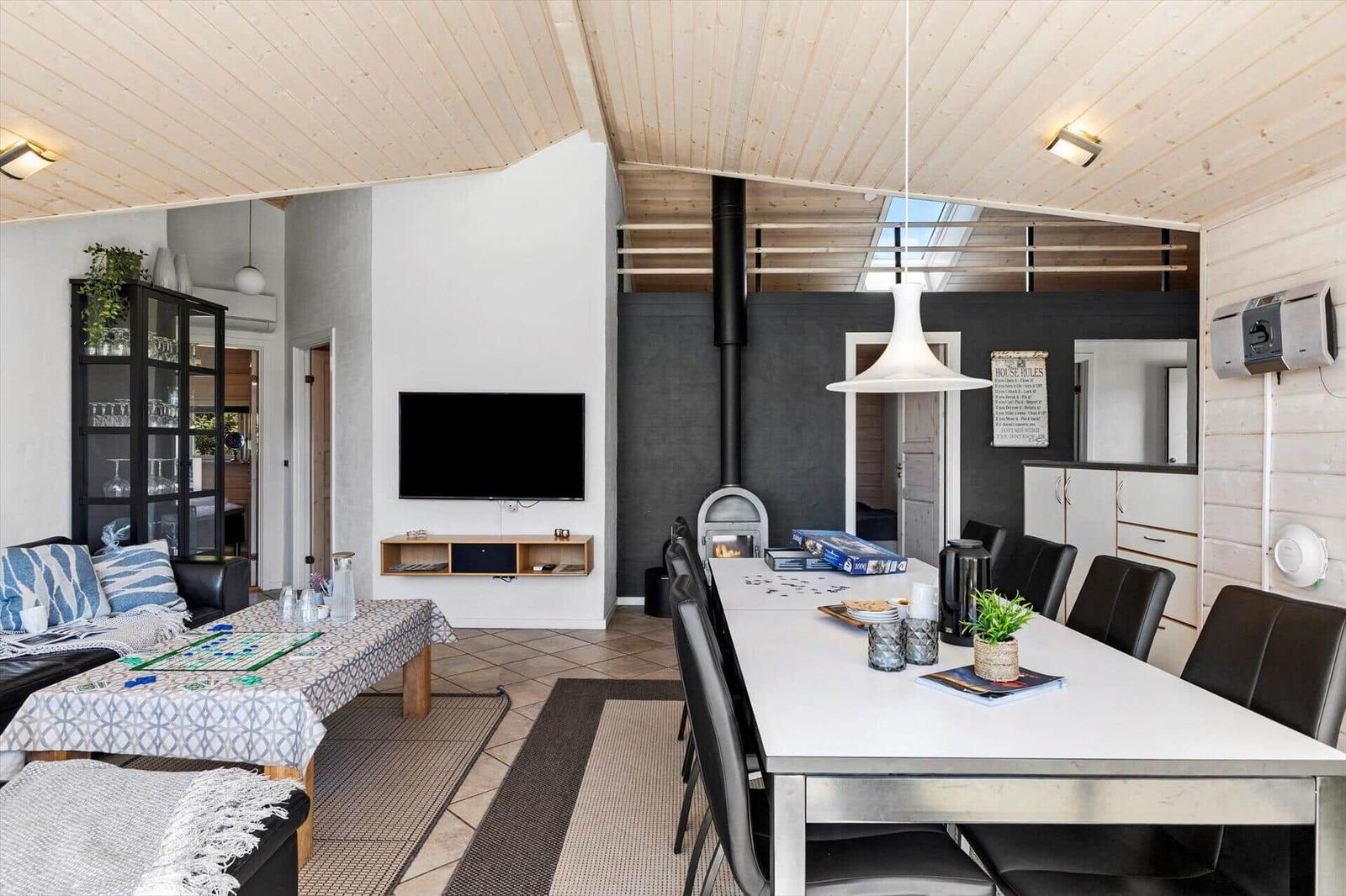 Wohn- und Essbereich mit Esstisch, Sofa und Kaminofen unter Holzdecke.