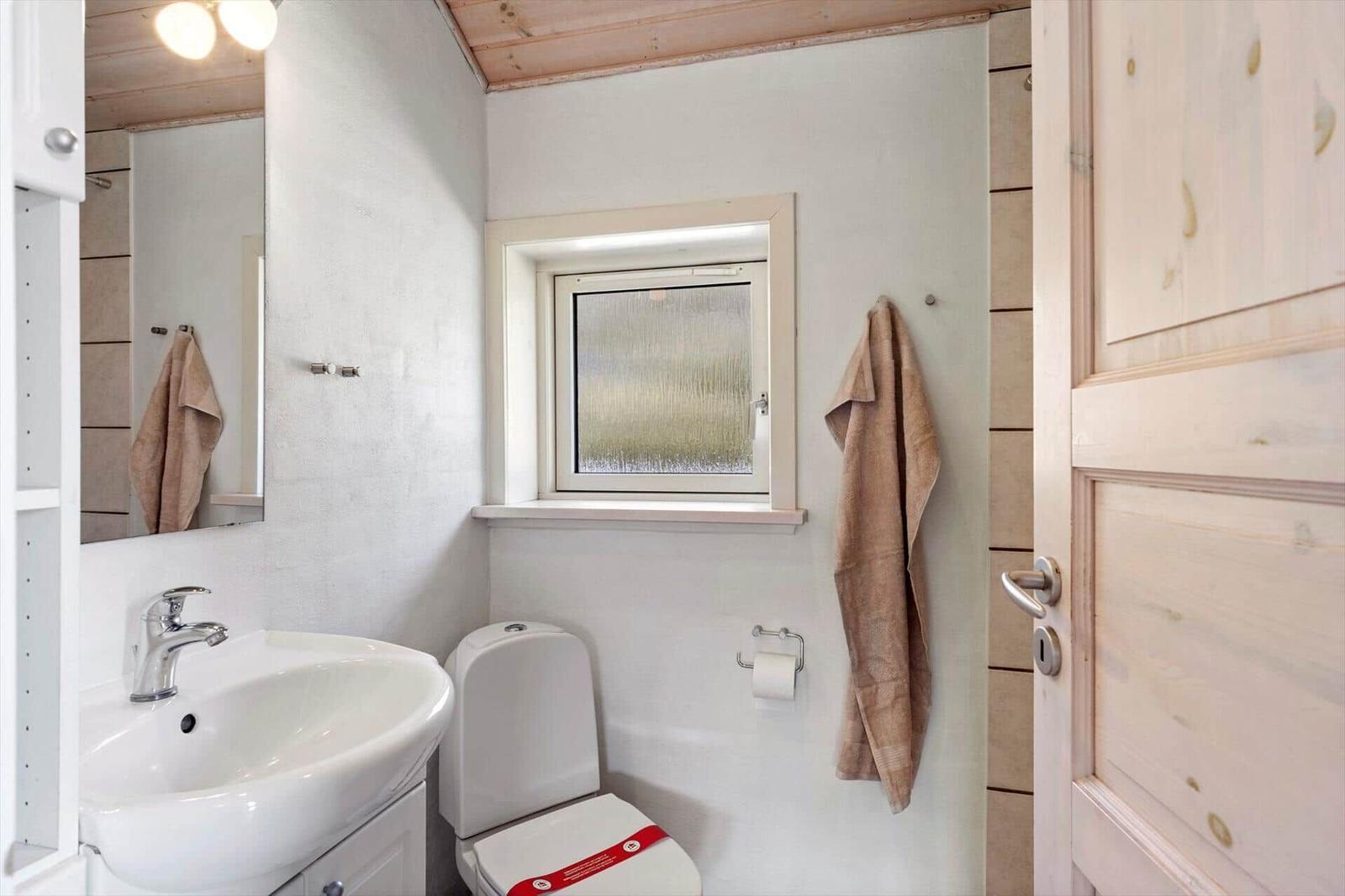 Badezimmer mit Waschbecken, Toilette und Fenster. Handtuch hängt an Wand.
