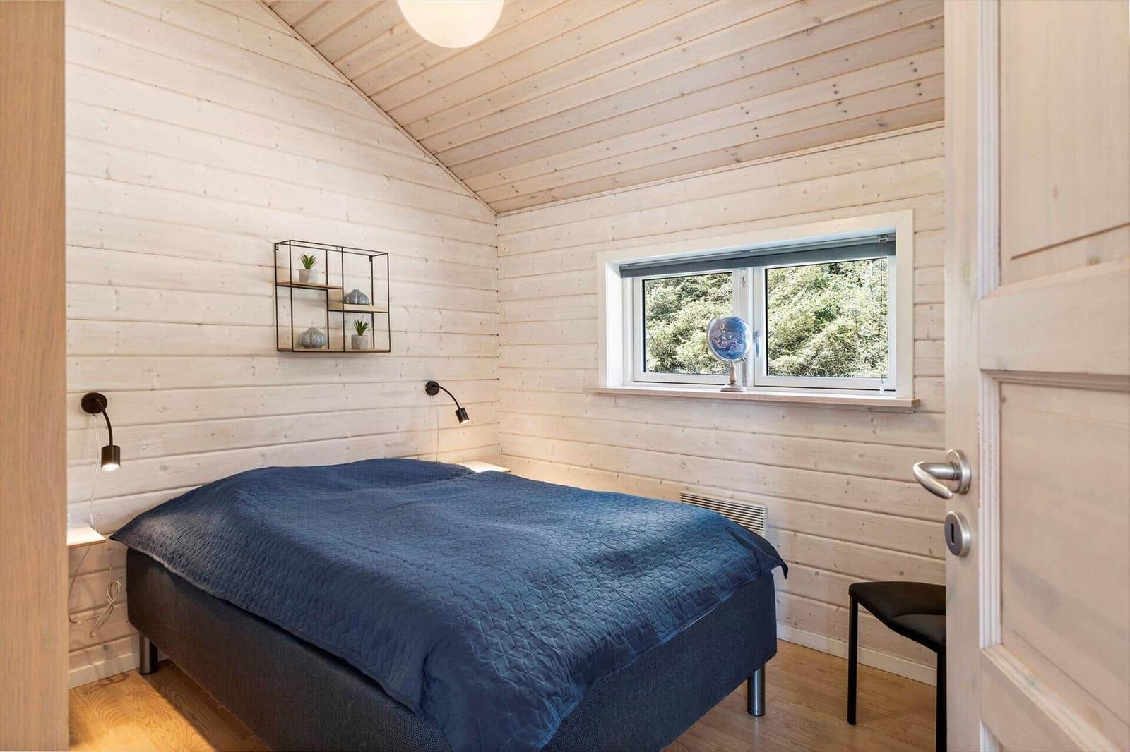 Schlafzimmer mit Holzwand, Bett und Fenster mit Blick auf Wald.