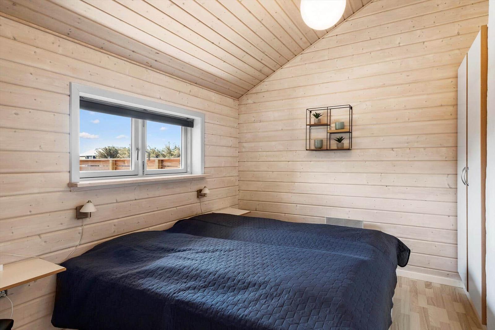Schlafzimmer mit Holzwand, Bett und Fenster. Wandregal mit Pflanzen.