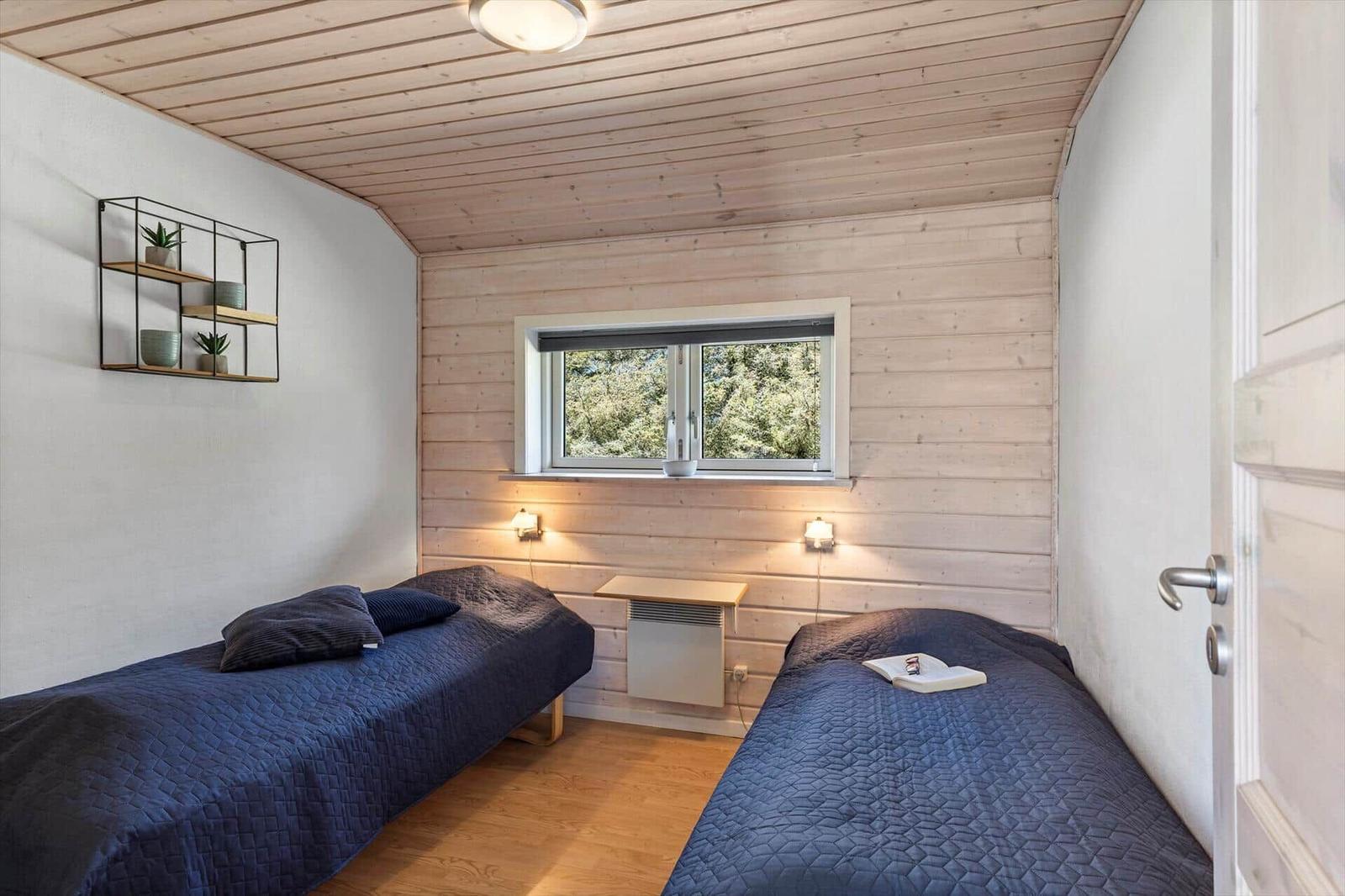 Zwei Einzelbetten, Holzwände, Fenster mit Blick auf Bäume und Wandregal mit Pflanzen.