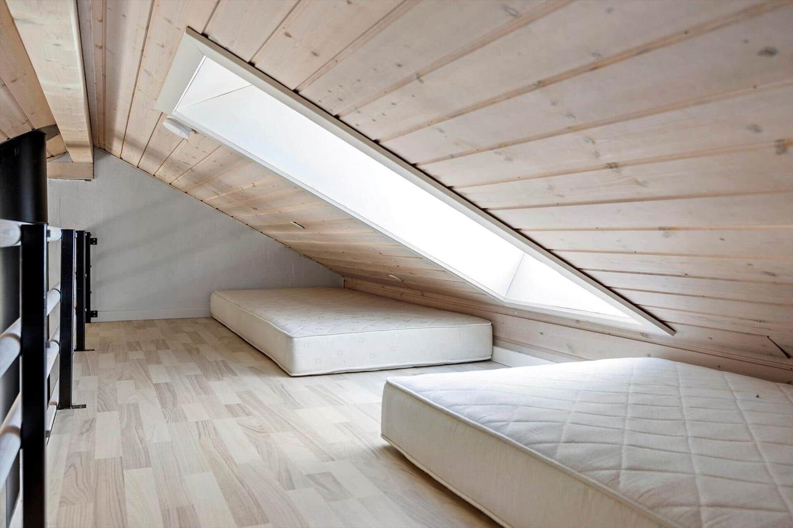 Zimmer mit zwei Matratzen und Dachfenster unter Holzdecke.