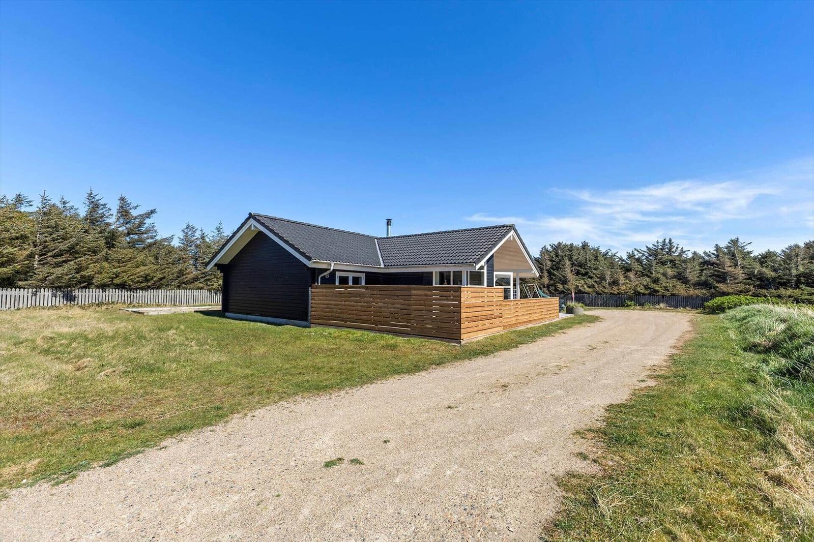 Moderne Holzhütte mit Terrasse und Gartenweg. Umgeben von Bäumen und Gras.