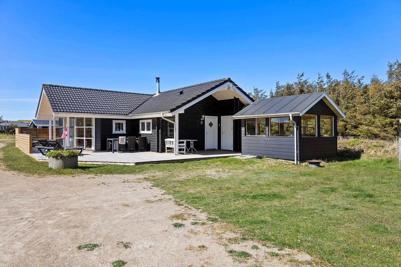Modernes Ferienhaus mit Terrasse, Garten und Grillplatz unter blauem Himmel.