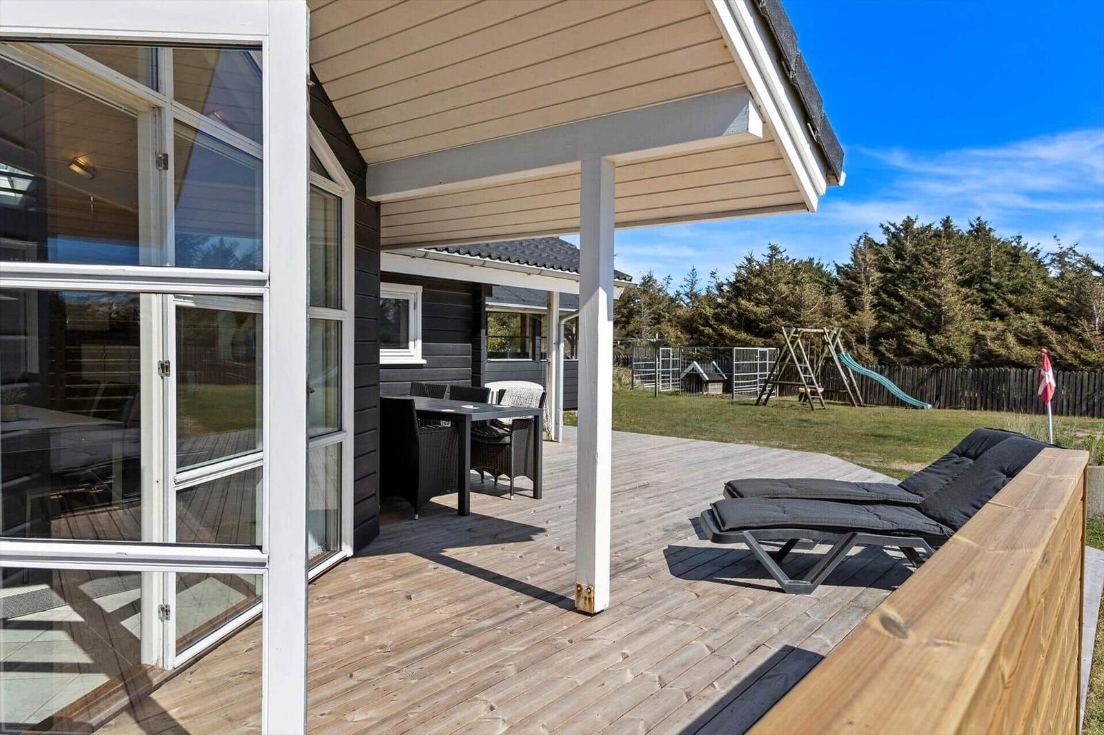 Terrasse mit Liegestühlen, Tisch und Gartenbereich mit Spielplatz.