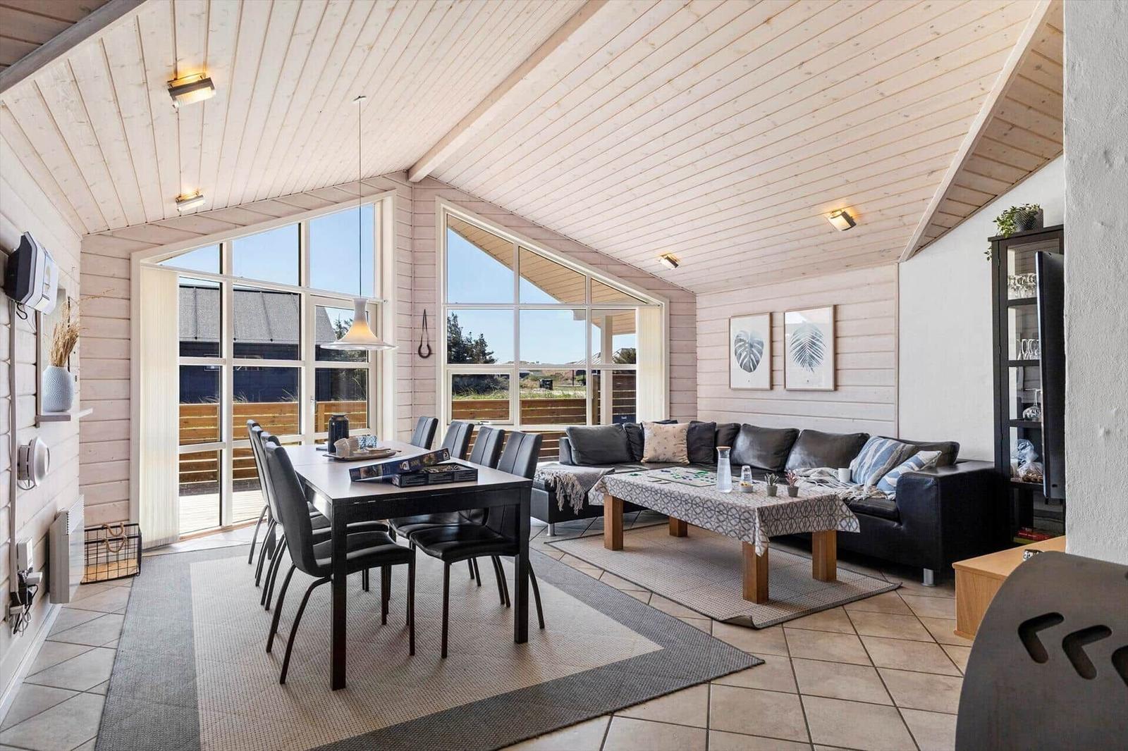 Wohn- und Essbereich mit Holzdecke, großen Fenstern und dunklem Sofa.