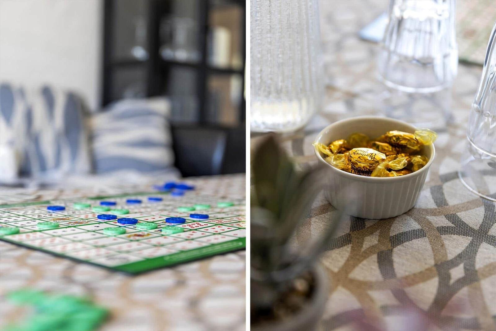 Ludo-Spiel auf Tisch mit blauen und grünen Spielsteinen. Tisch mit Schale voller goldverpackter Schokolade.