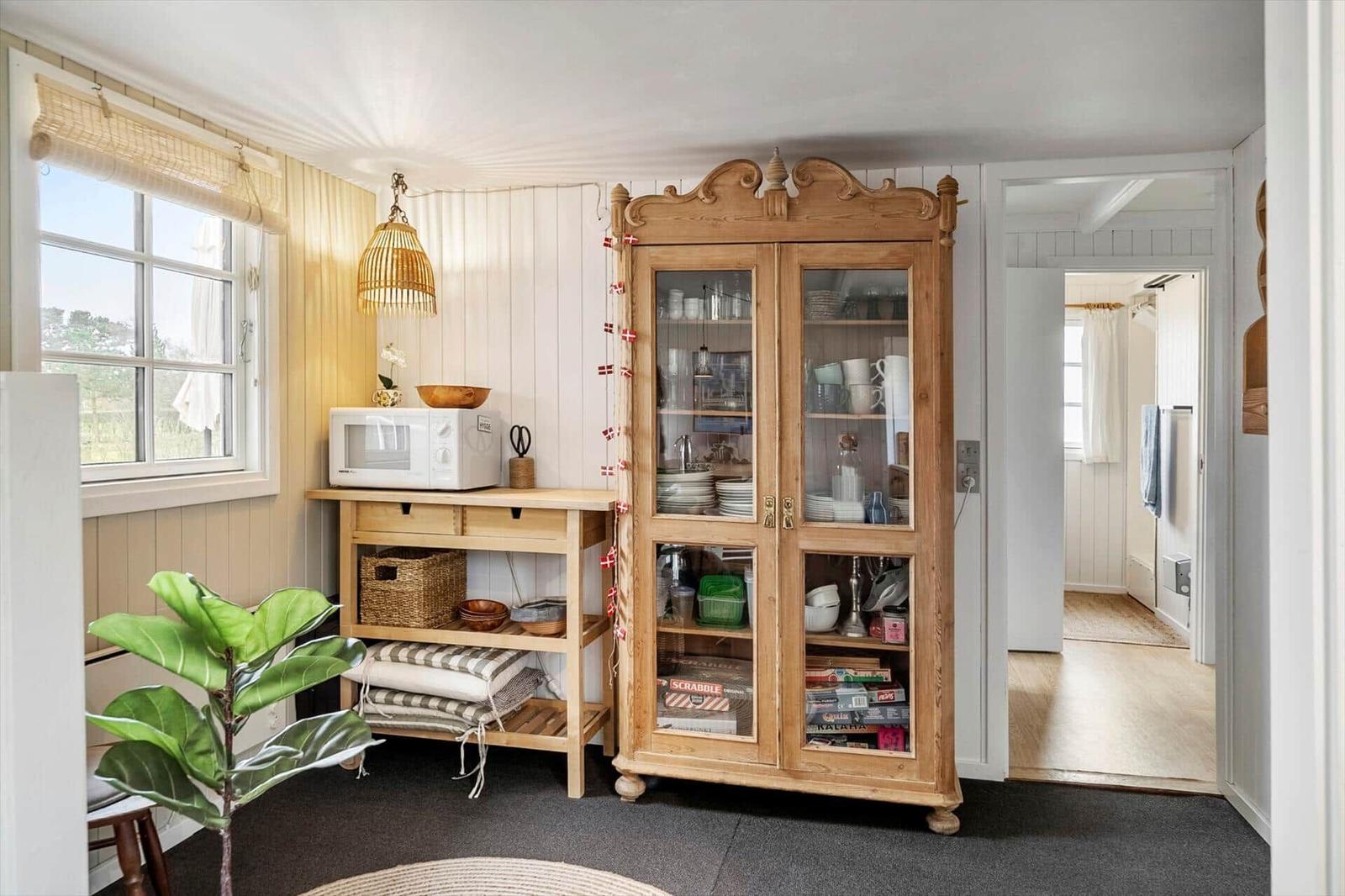 Küchenbereich mit Holzschrank, Mikrowelle und Fenster.