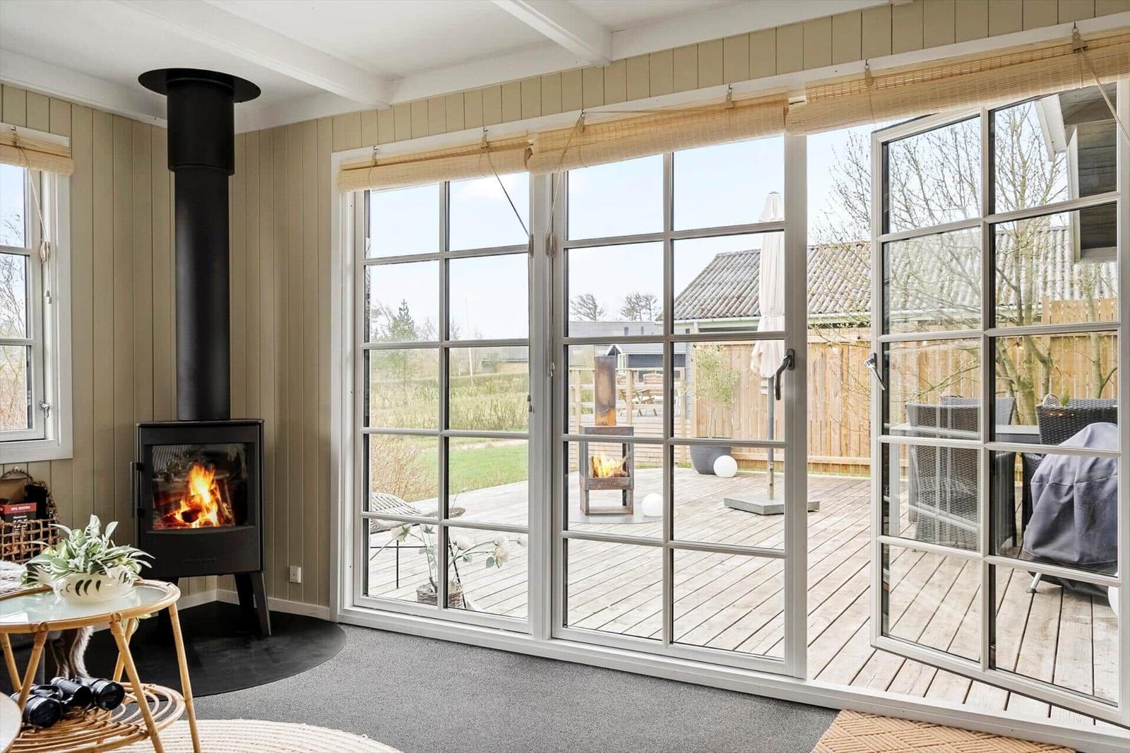 Ein Raum mit Kamin, großen Fenstern und Blick auf eine Terrasse mit Garten.