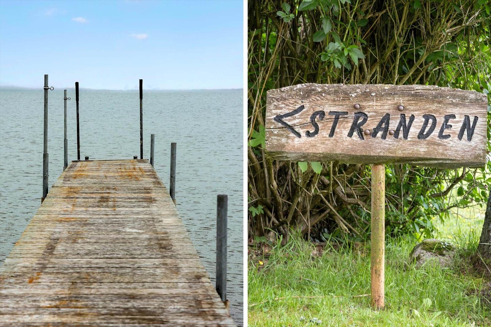 Holzsteg führt zum Wasser. Schild weist auf Strand hin.