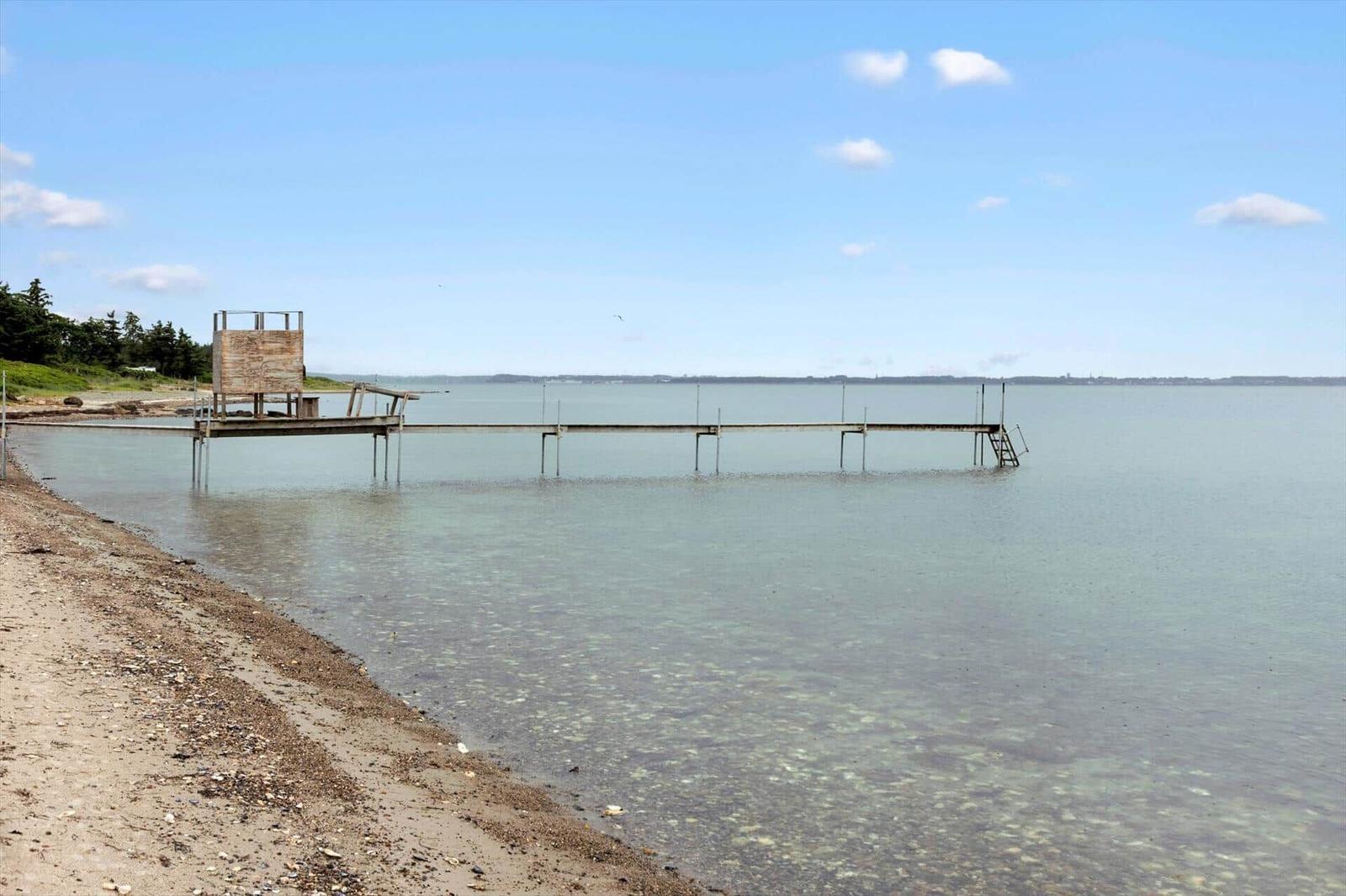 Holzsteg mit Dusche am Strand. Klare See. Himmel mit Wolken.