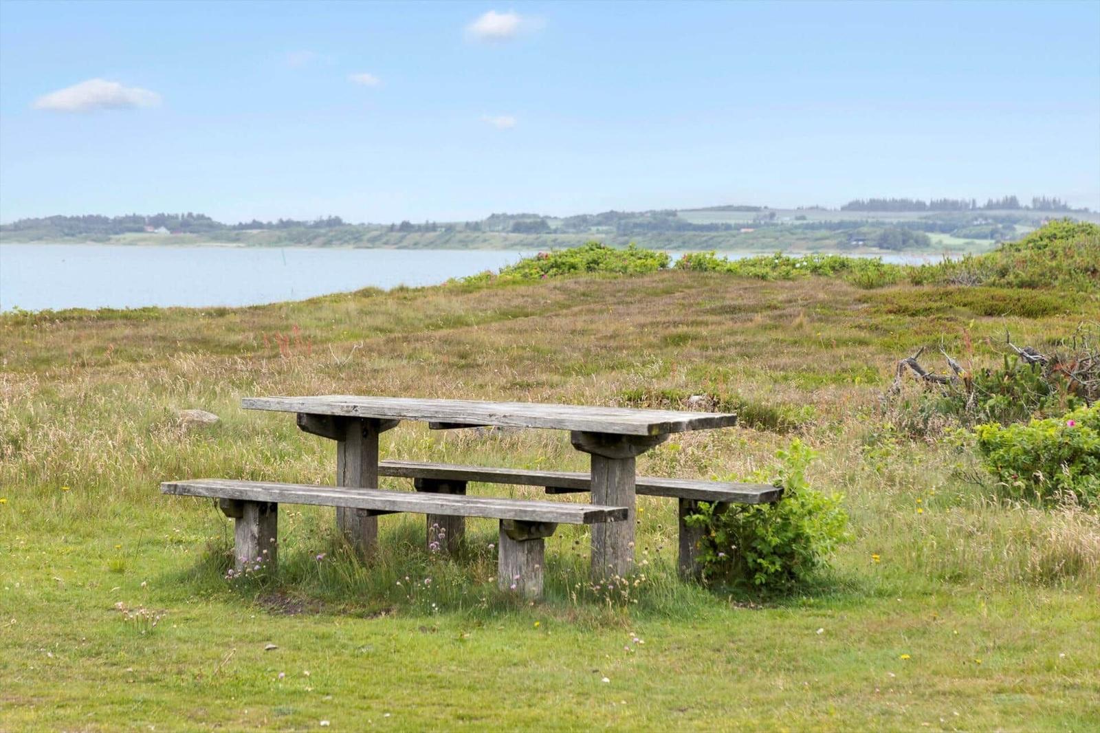 Holzbank und Tisch auf grünem Rasen mit Blick auf Wasser und Hügel.
