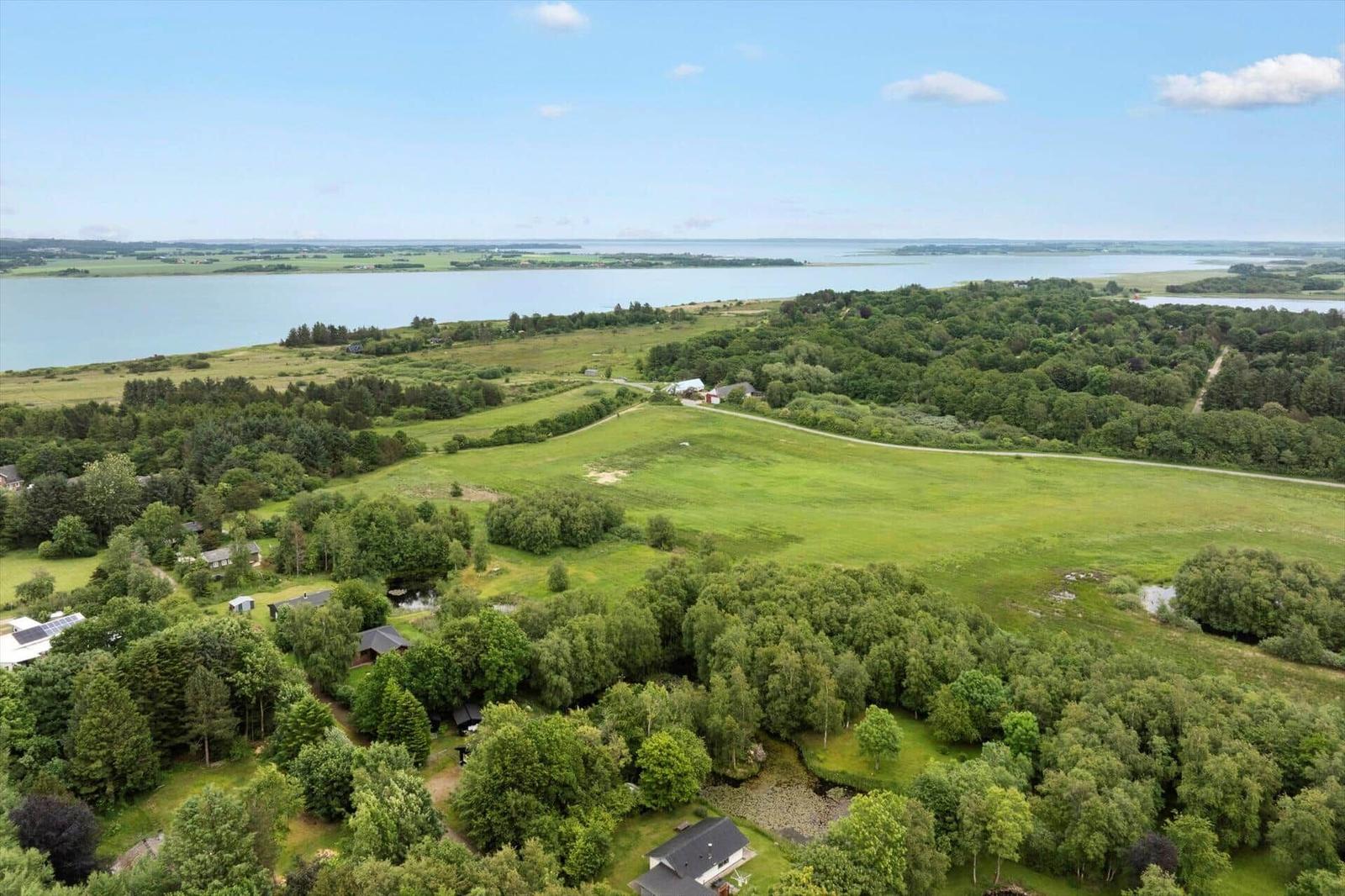 Weitläufige grüne Landschaft mit Wald, Feldern und einem See im Hintergrund.