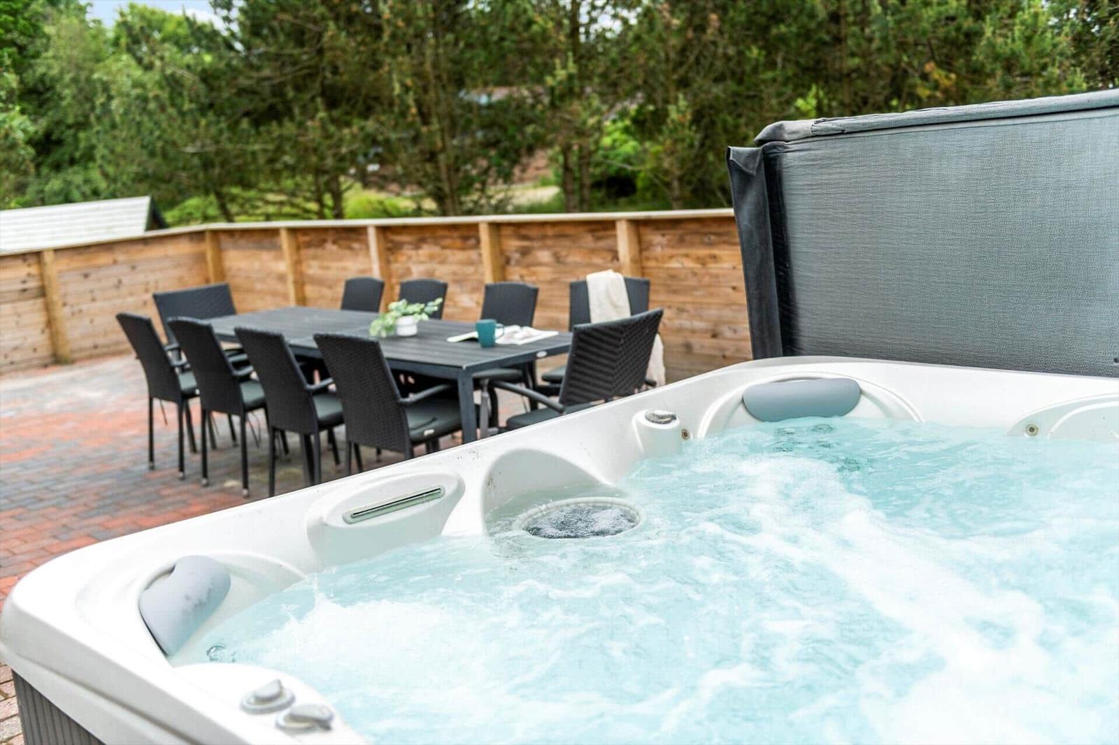 Eine Whirlpoolbadewanne auf einer Terrasse mit Gartenmöbeln und Holzzaun im Hintergrund.