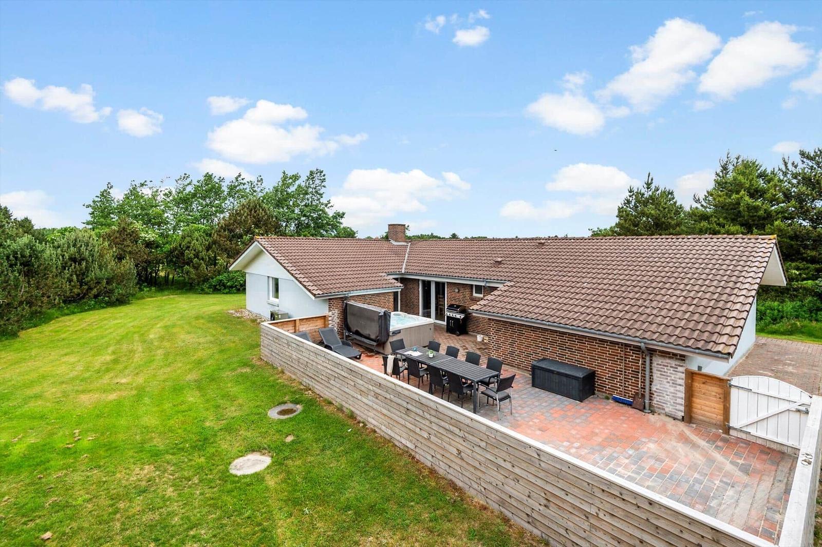 Haus mit Terrasse, Grill und Whirlpool im Garten. Umgeben von Gras und Bäumen.