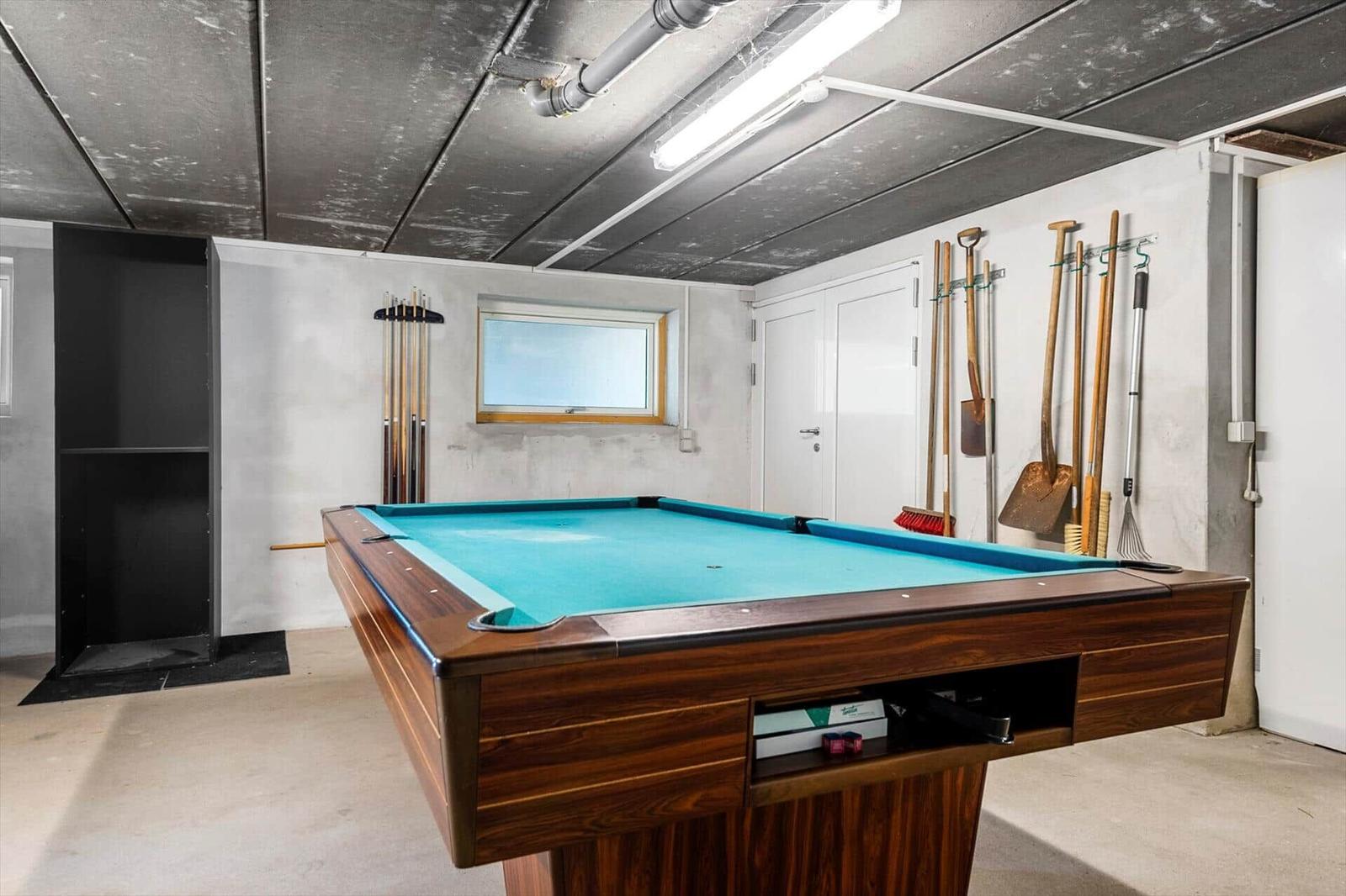 Billiard table with blue felt and wooden frame in a room with tools on the wall.