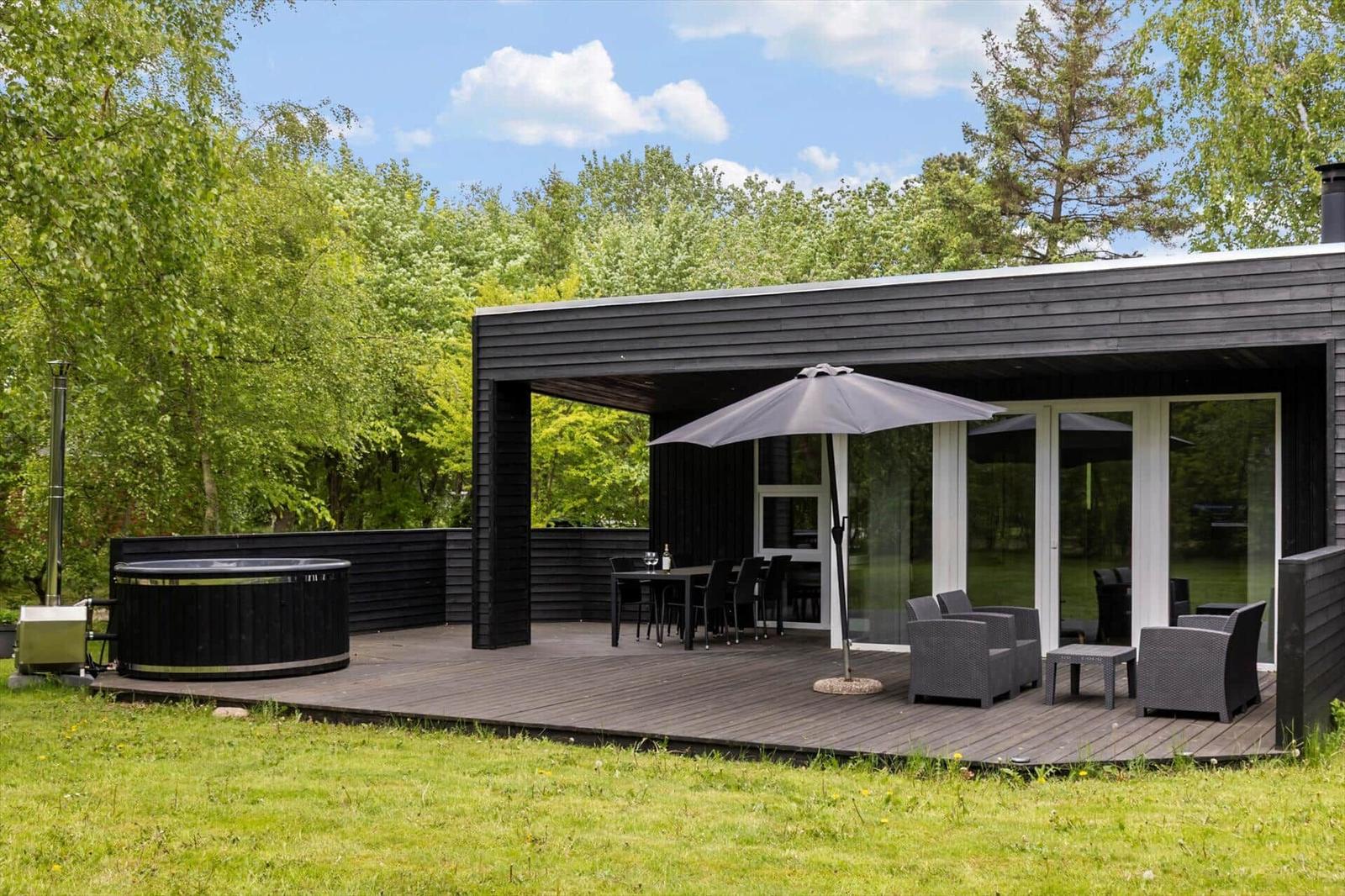 Terrasse mit Hot Tub, Sitzgruppe und Tisch unter einem Sonnenschirm.