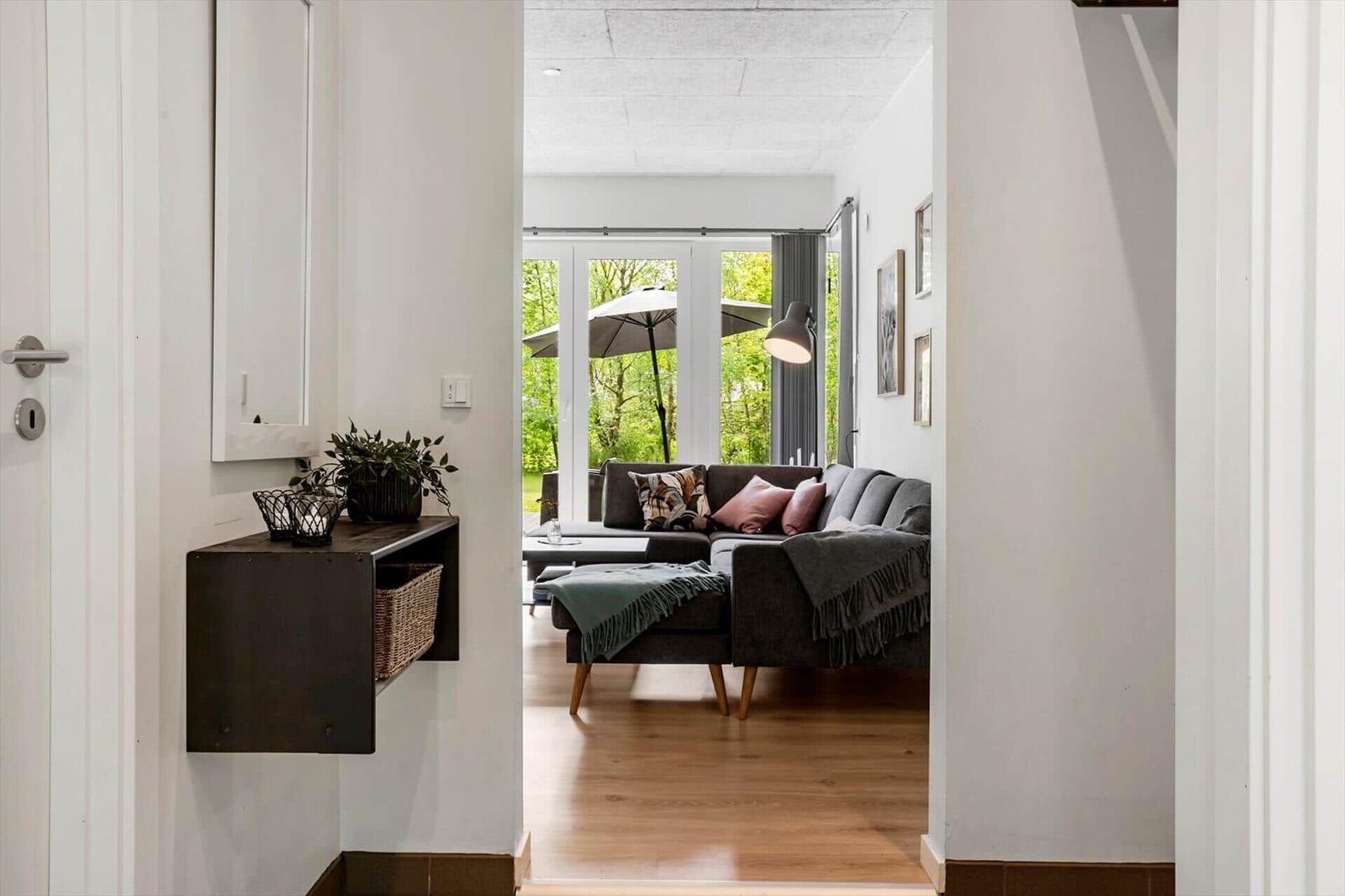 Eingangsbereich mit Wandregal und Blick in Wohnzimmer mit Sofa und Terrasse.