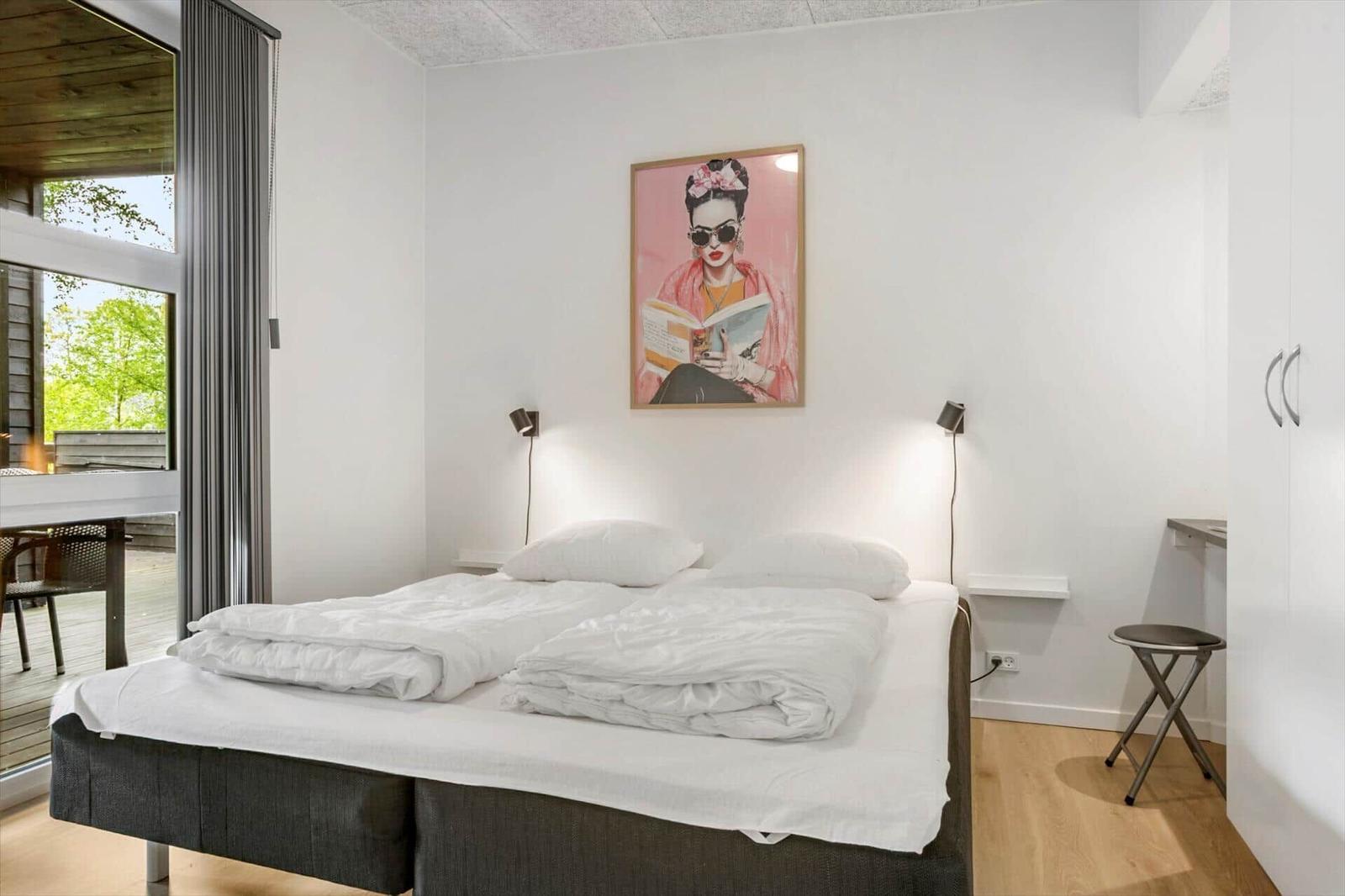 Schlafzimmer mit Doppelbett, Wandbild und Blick auf Terrasse.