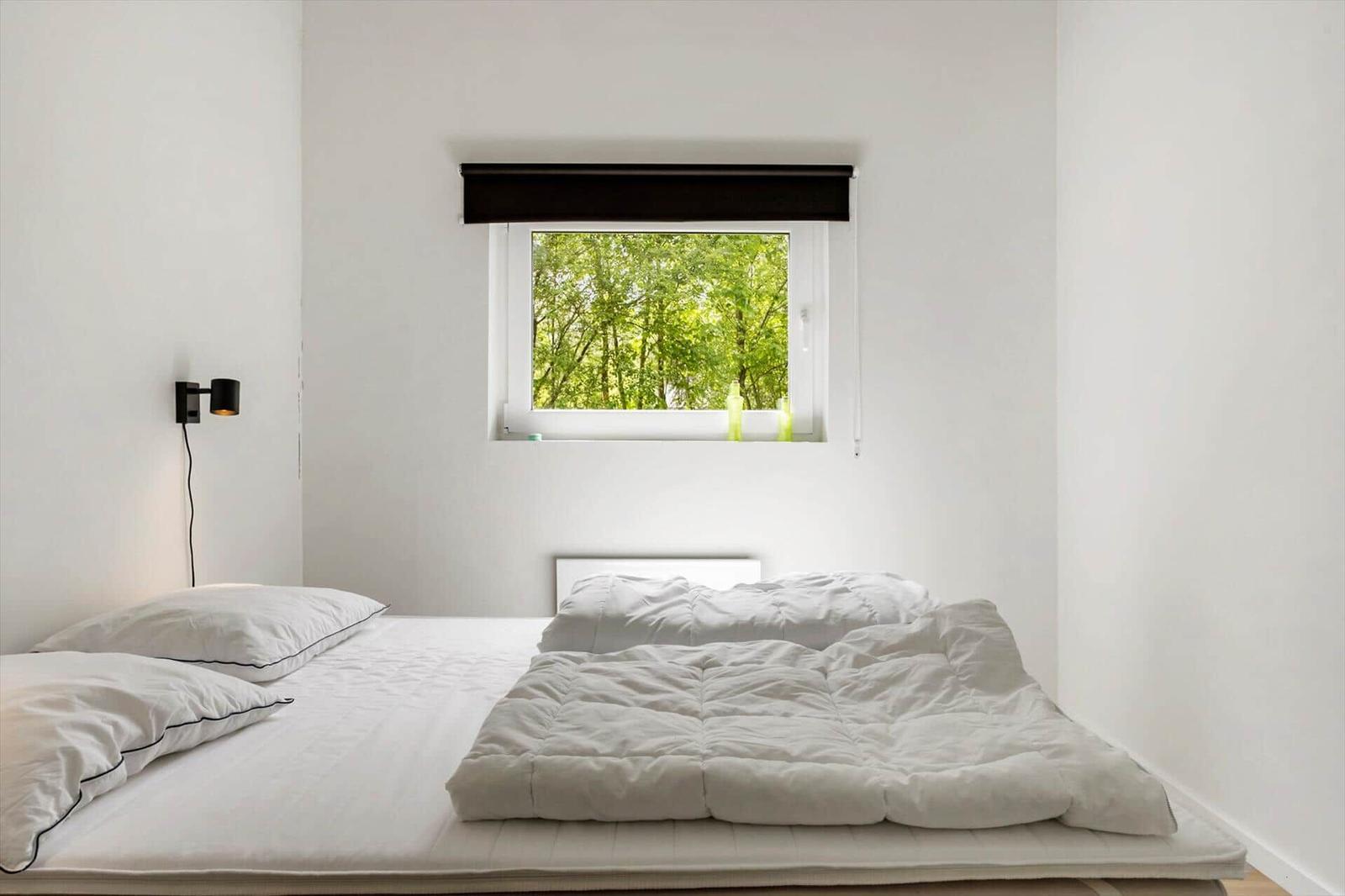 Schlafzimmer mit Bett, Fenster und Wandlampe.