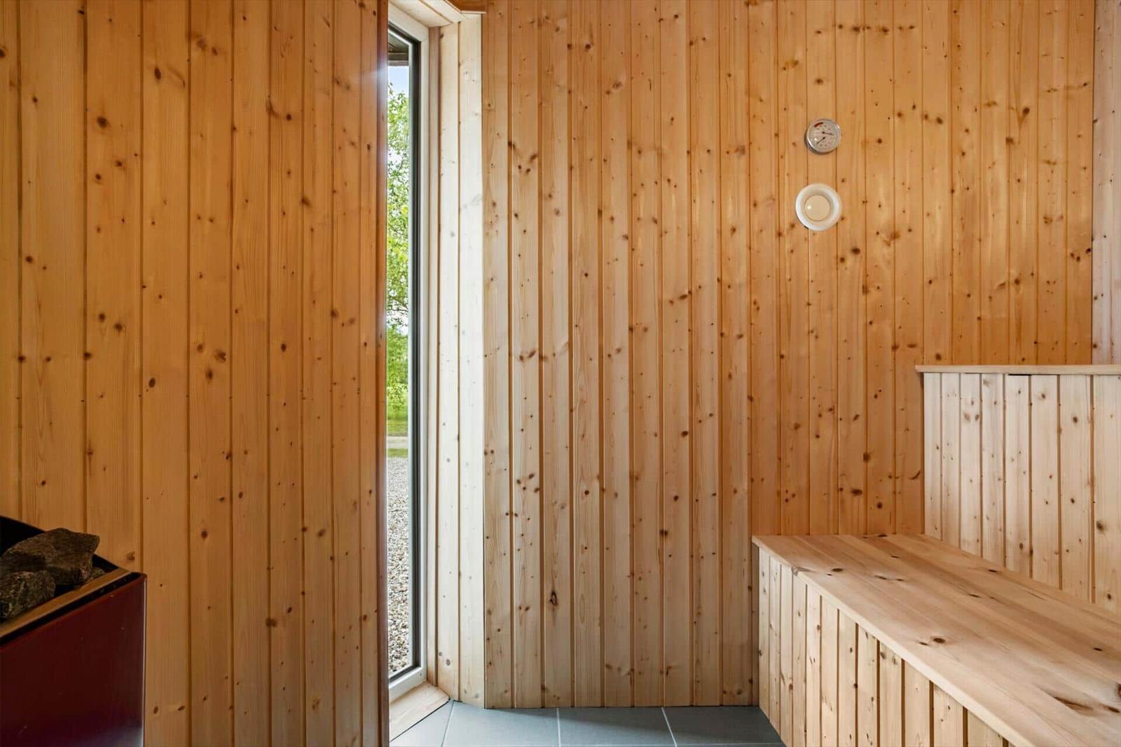 Sauna mit Holzwänden, Sitzbank und Fenster. Thermometer und Lichtschalter an der Wand.