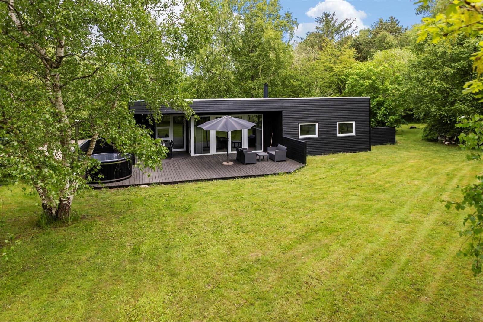 Moderne schwarze Hütte mit Terrasse, Sitzgelegenheit und Whirlpool im Grünen.