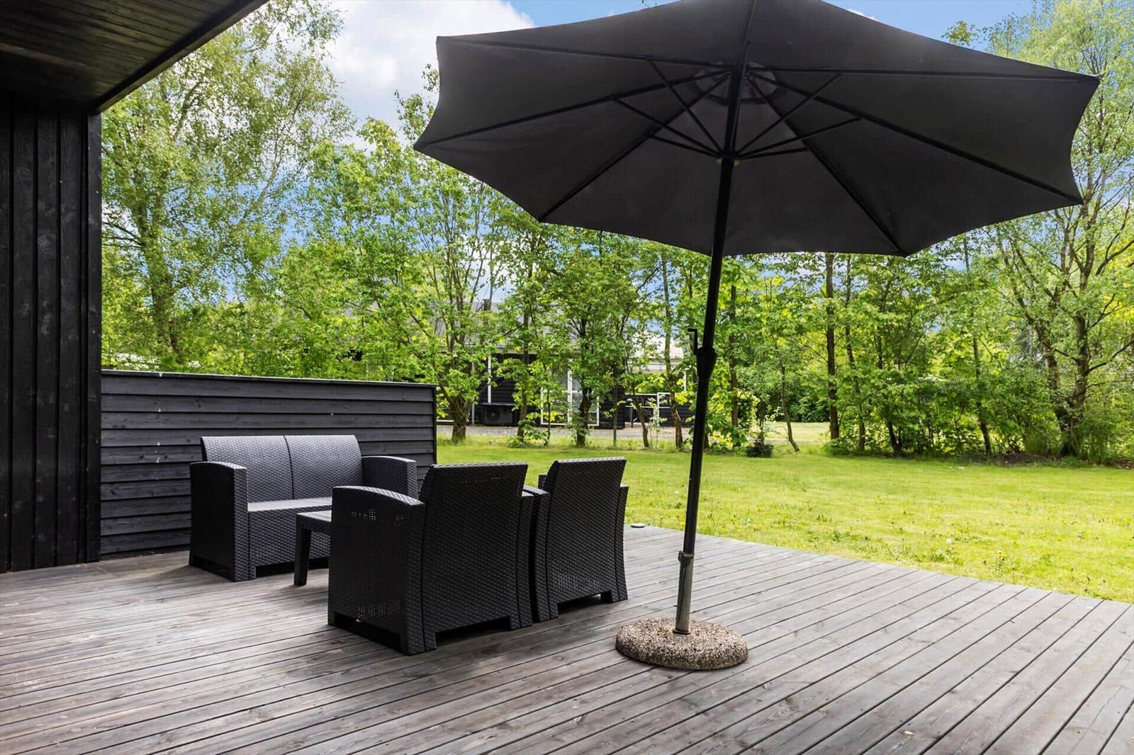 Terrasse mit Sitzgruppe und Sonnenschirm. Grünfläche und Bäume im Hintergrund.