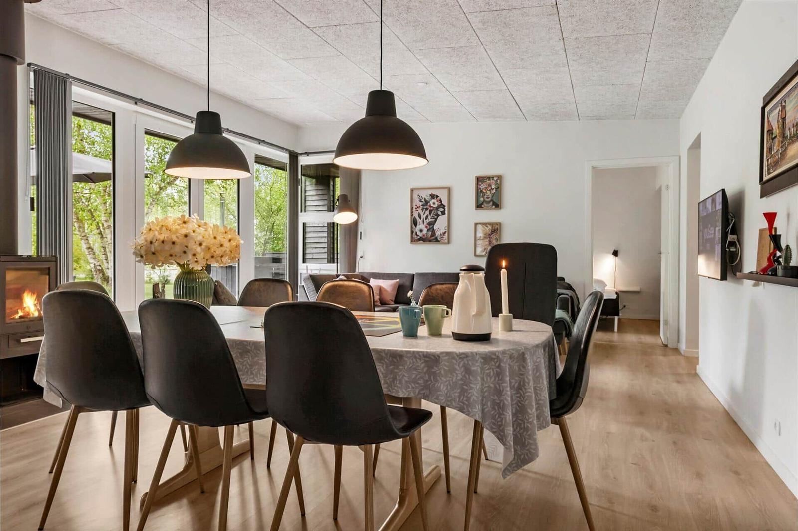 Esszimmer mit Tisch, Stühlen und Fenstern. Im Hintergrund Wohnbereich mit Sofa.