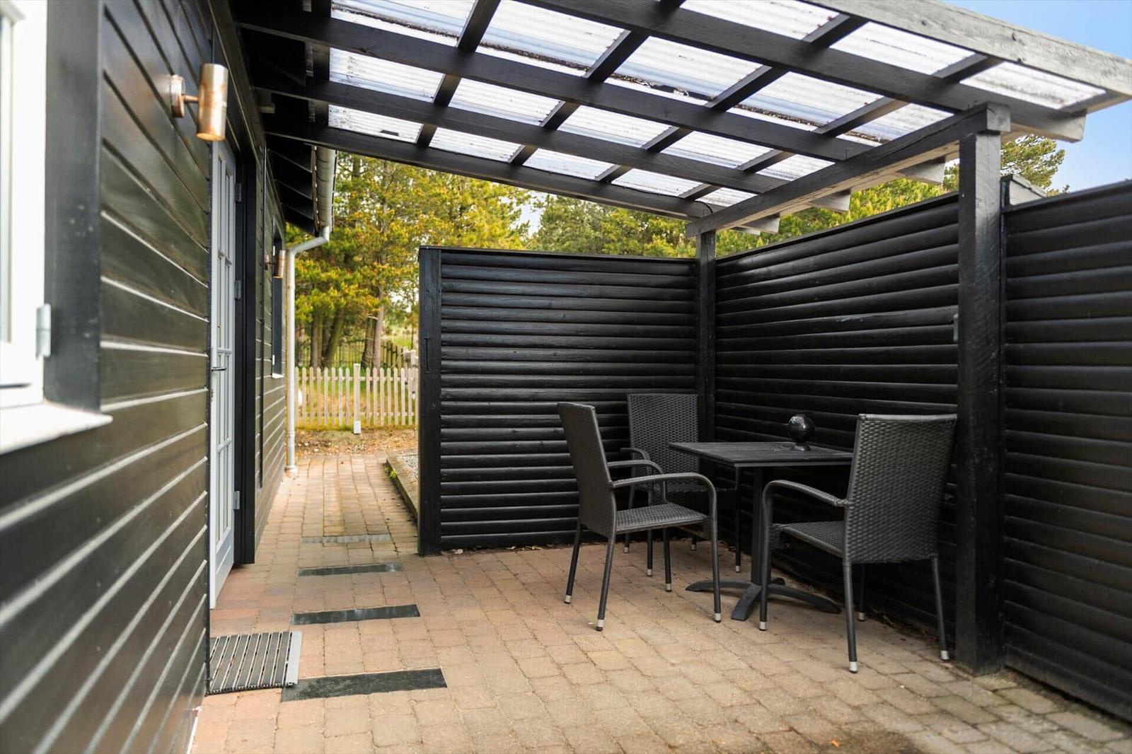 Terrasse mit Tisch und Stühlen unter einer Markise. Schwarze Holzwände und Terrassenplatten.