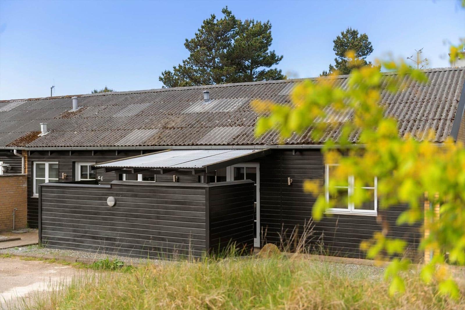 Moderne Holzhütte mit Dachüberdachung und Fenstern. Gras und Bäume im Hintergrund.