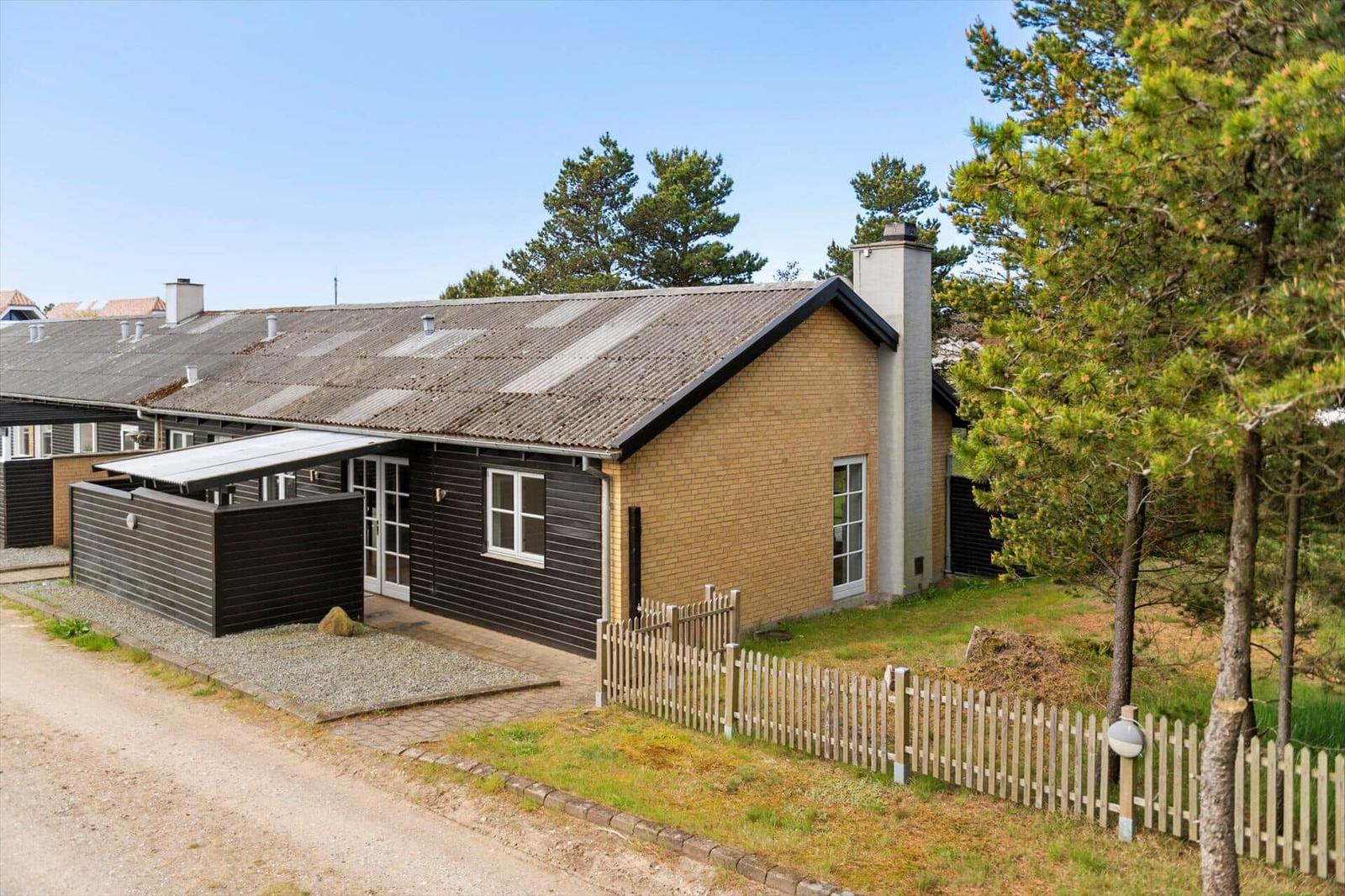 Ein modernes Haus mit braunem Ziegel und dunkler Fassade, umgeben von Bäumen und einem weißen Zaun.
