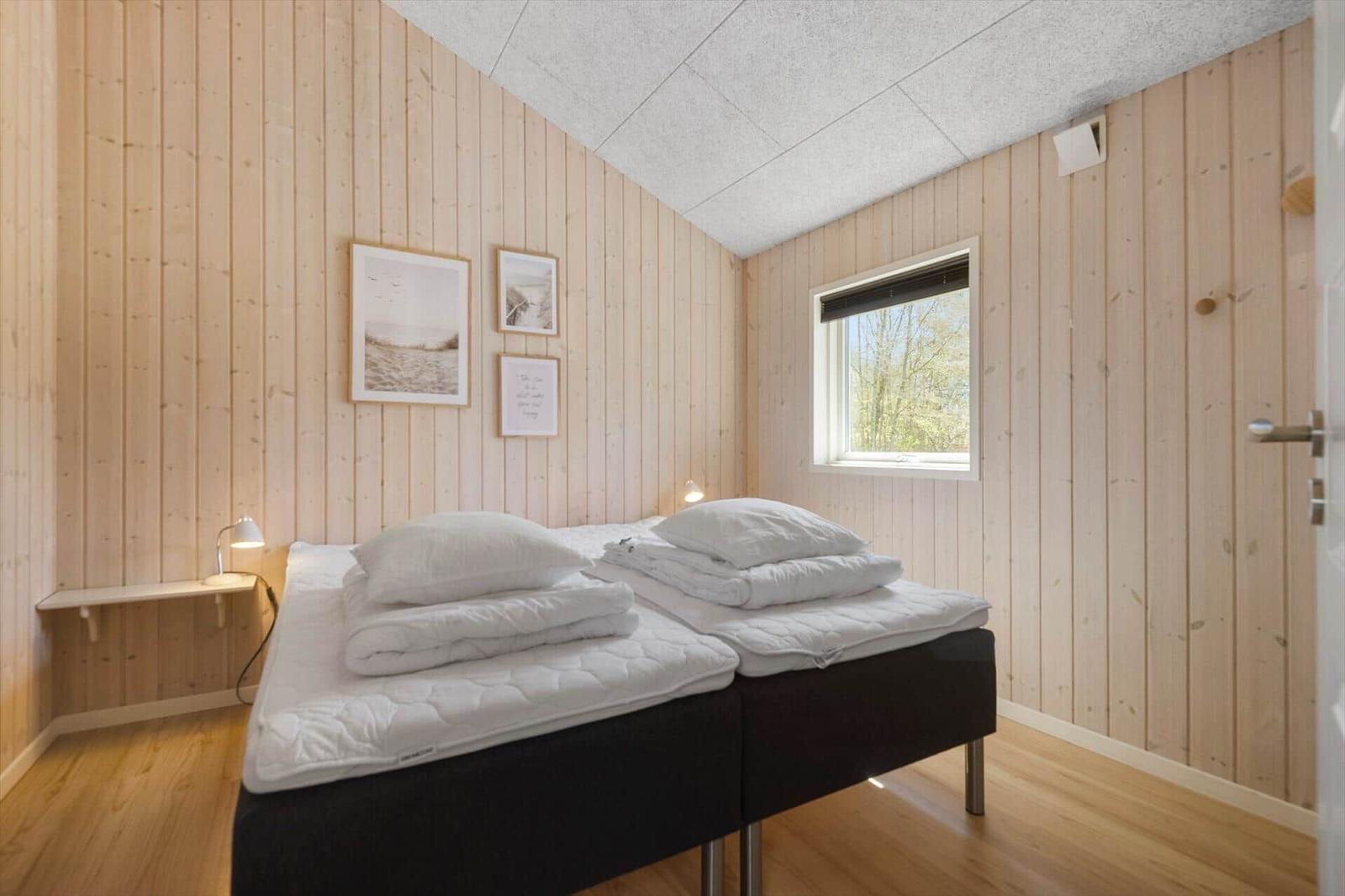 Schlafzimmer mit Holzwand, Bett und Fenster mit Blick auf Bäume.