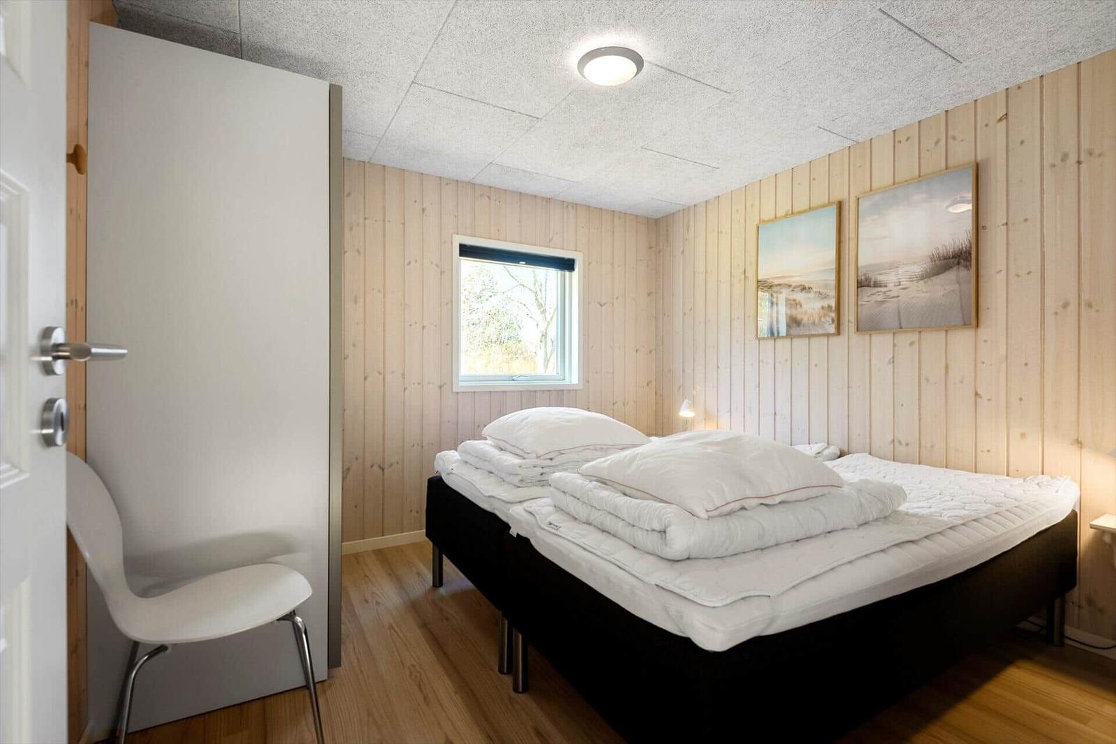 Schlafzimmer mit Holzwand, Bett, Fenster und zwei Bildern an der Wand.