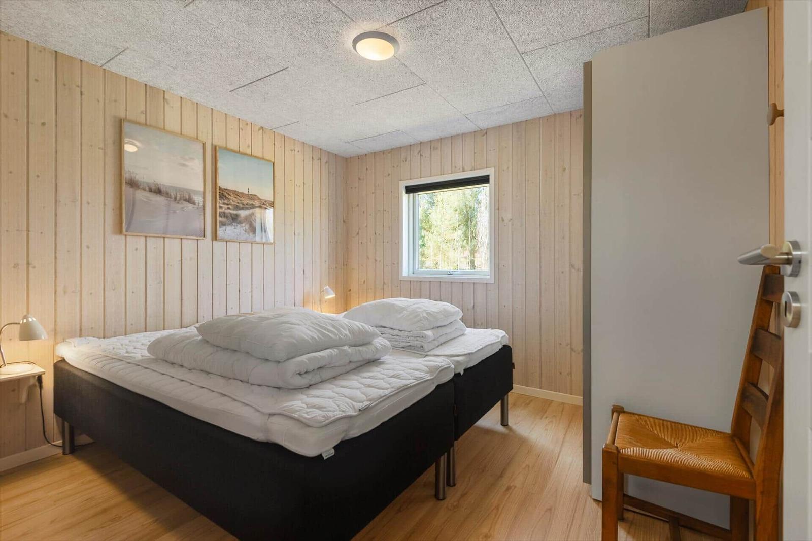 Schlafzimmer mit Holzwand, Bett, Fenster und Stuhl