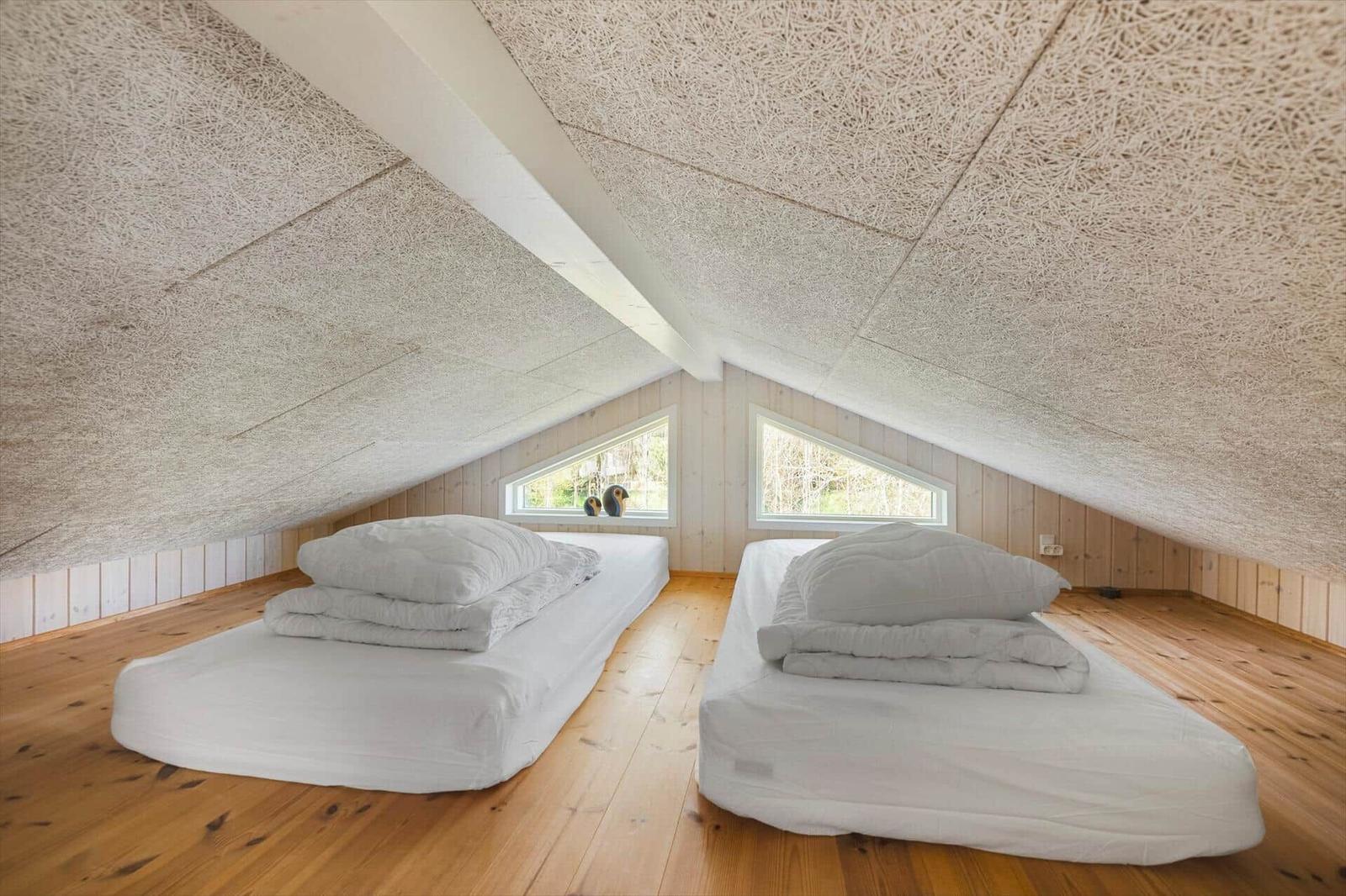 Zwei Matratzen auf Holzdielen, Dachschräge mit Textildecke, zwei Dreiecksfenster