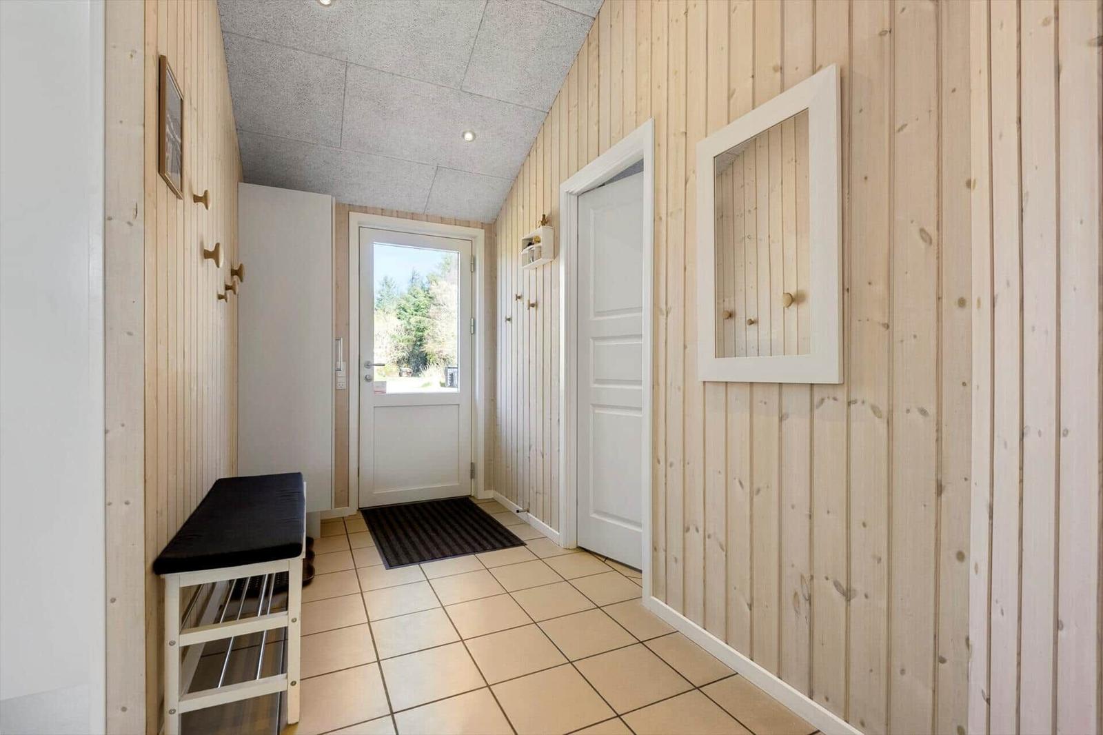 Hausflur mit Holzwand, Tür und Spiegel. Bodenfliesen und Sitzbank.