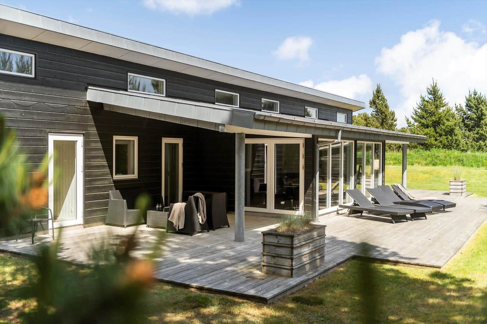 Moderne Villa mit Terrasse, Liegen und Garten. Große Fenster und schwarz lackierte Fassade.