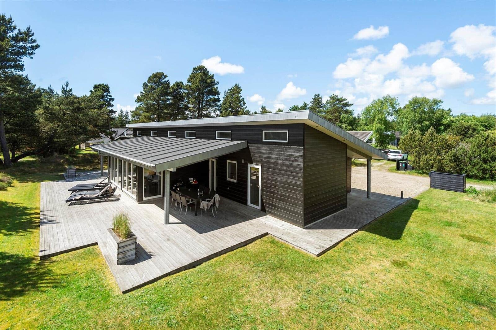 Moderne Holzhütte mit großem Holzterrasse, Garten und Blick auf Bäume.