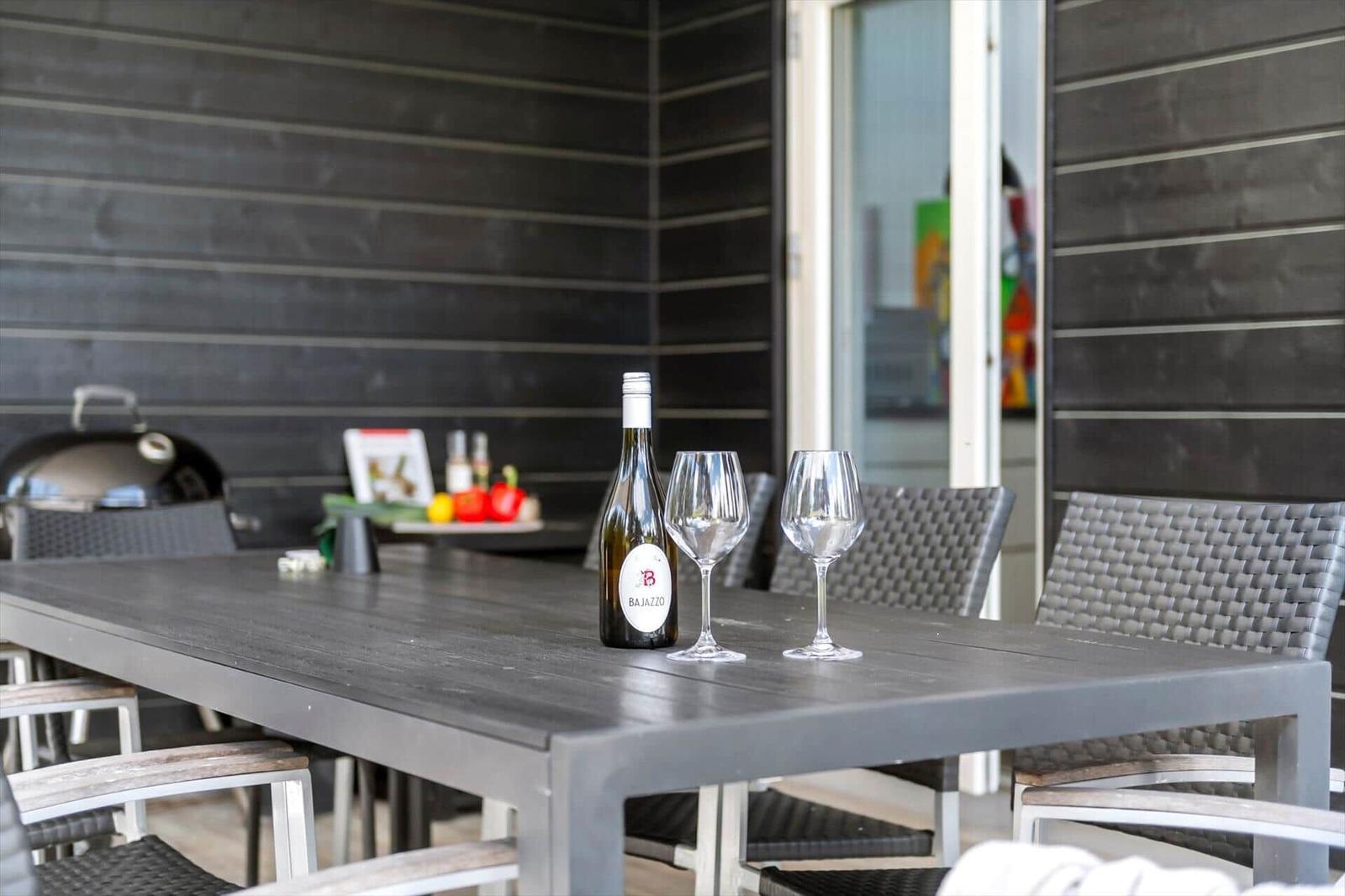 Außenbereich mit Tisch, Stühlen, Grill und Weinflasche.