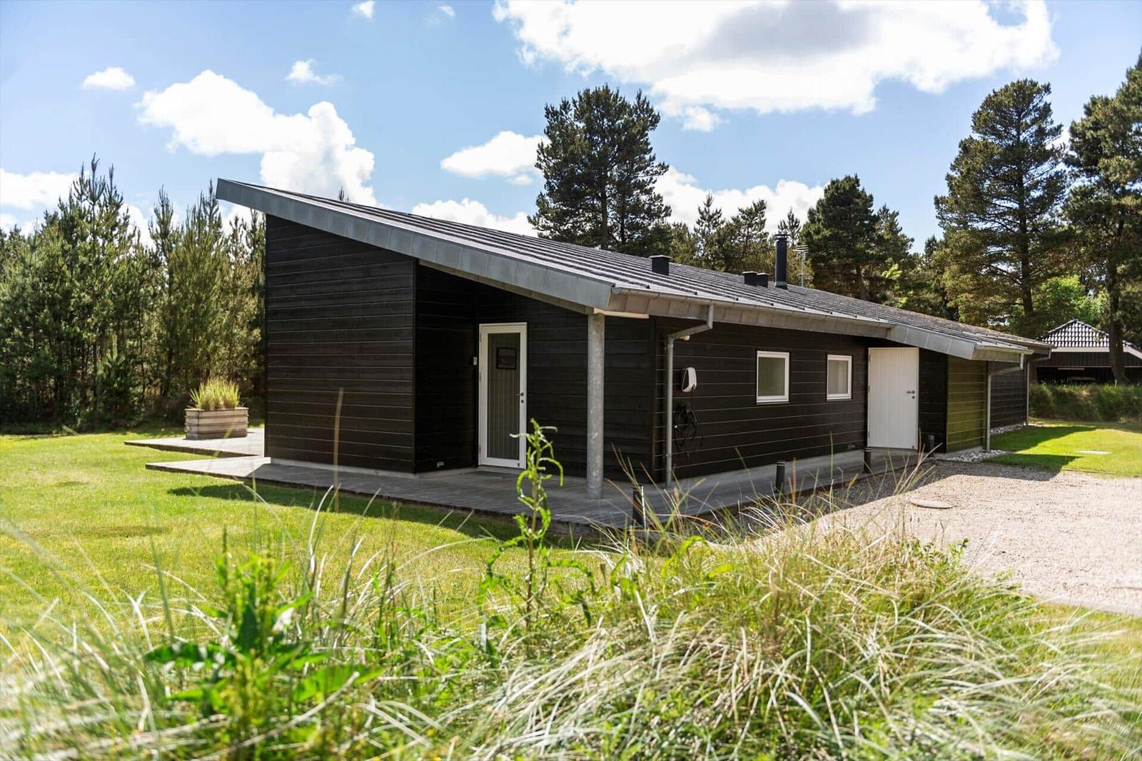 Moderne Holzhütte mit Terrasse und Garten. Umgeben von Bäumen unter blauem Himmel.