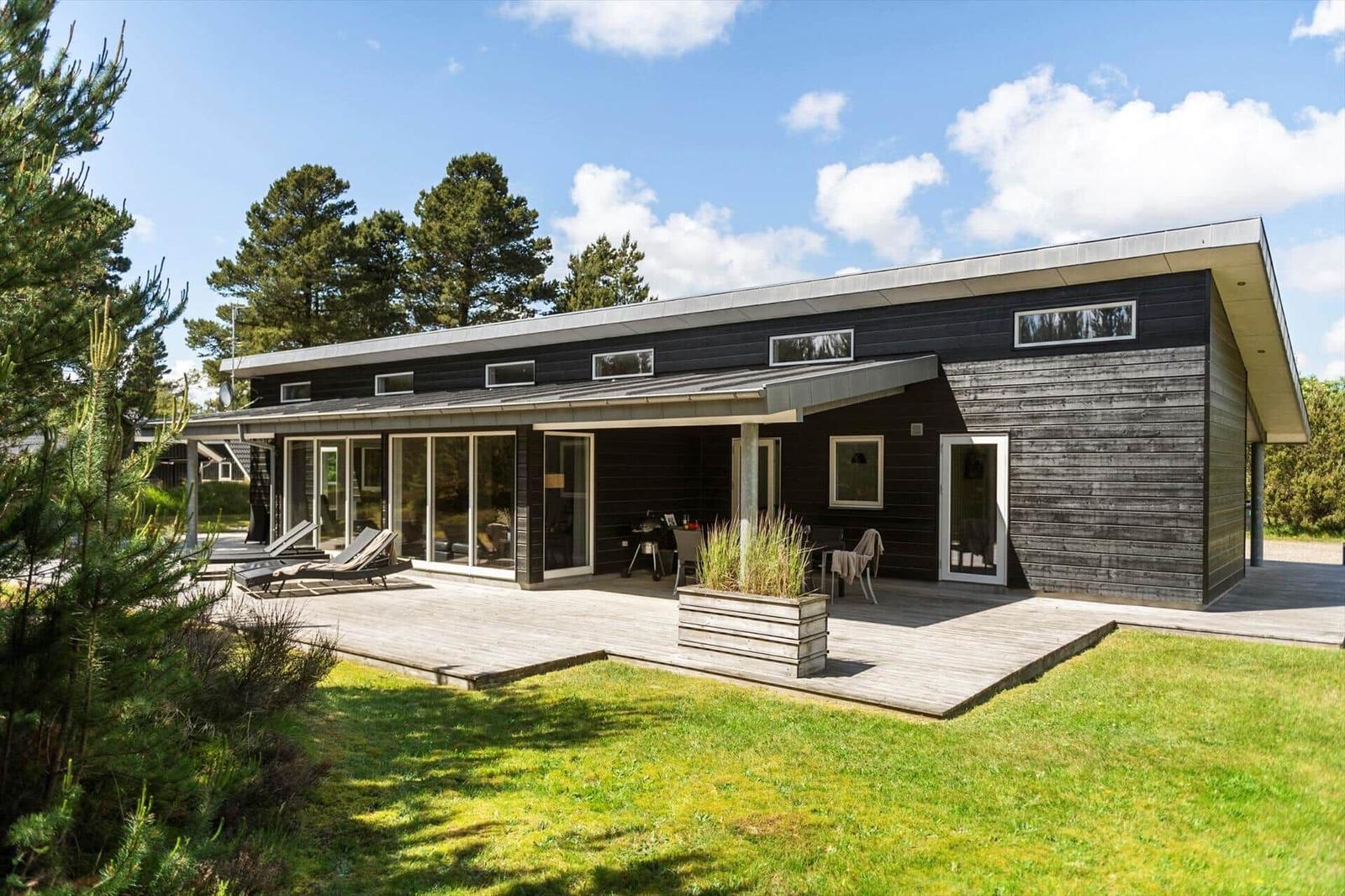 Moderne Villa mit Terrasse, Garten und Blick auf Bäume unter blauem Himmel.