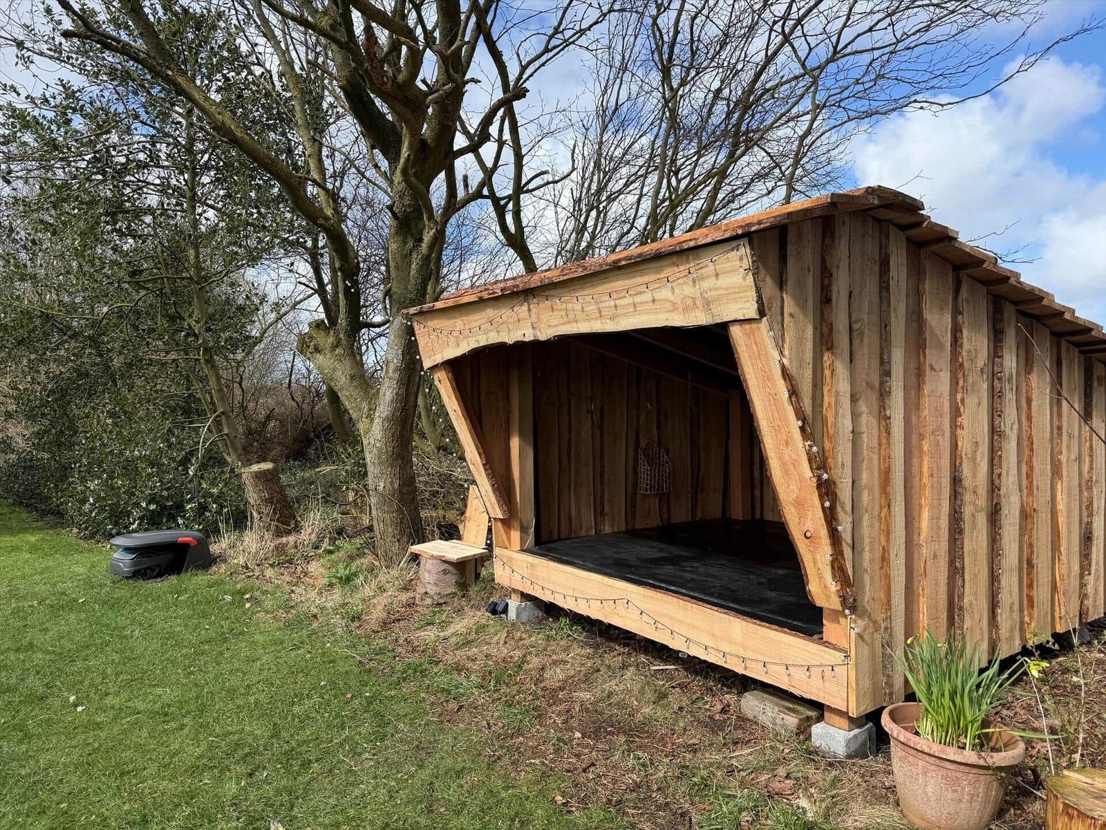 Wooden structure with open front and floor area outdoors.