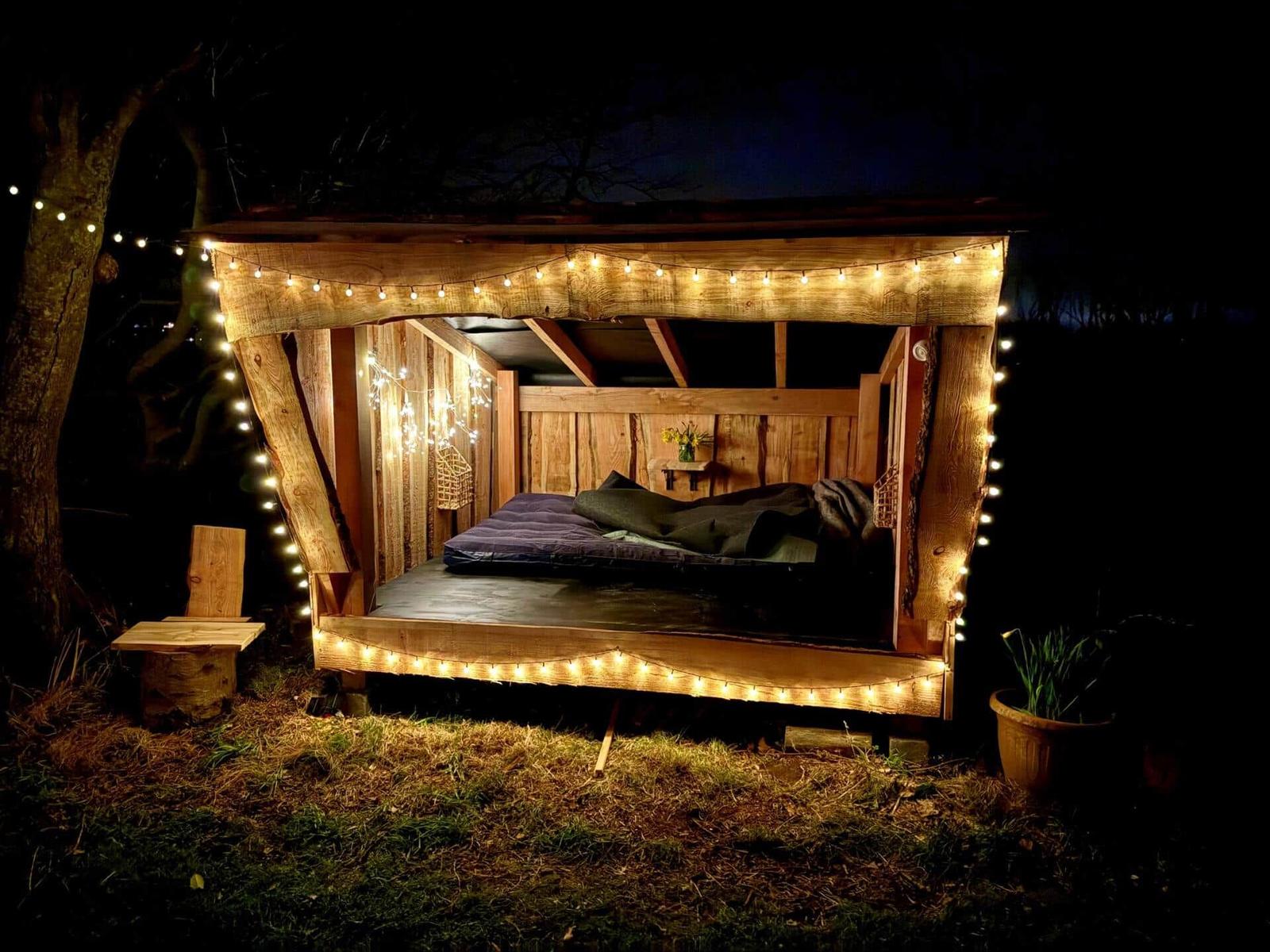 Wooden structure with mattress and string lights outdoors at night.