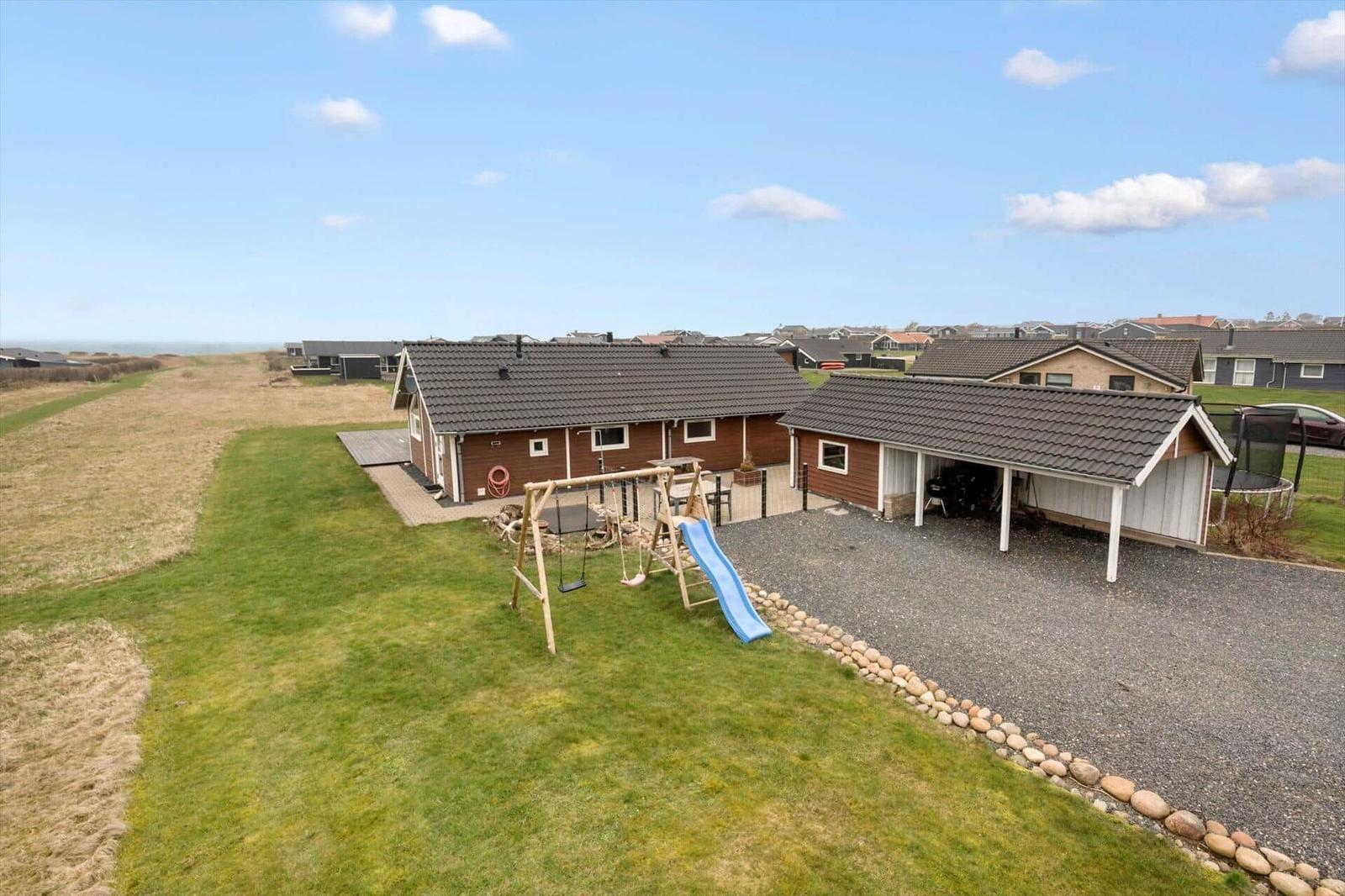 Holzhaus mit Spielplatz und Garage auf grünem Grundstück.