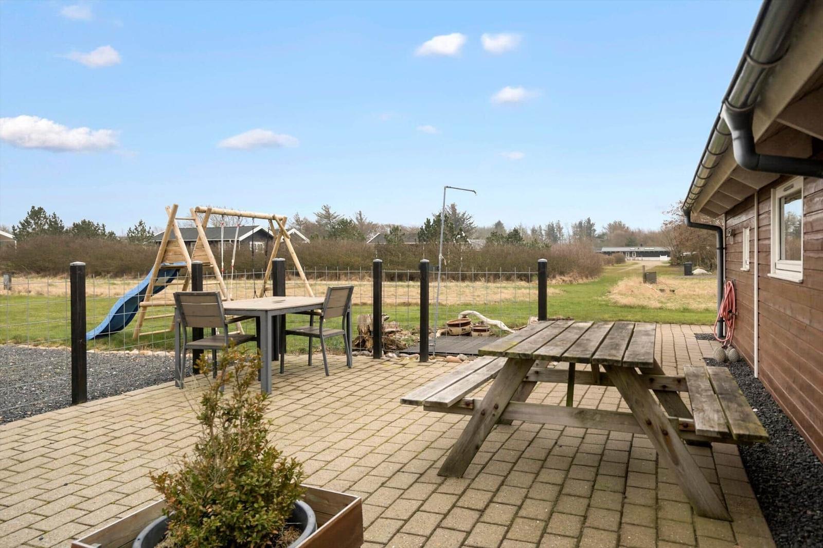 Terrasse mit Picknicktisch, Tisch und Stühlen, Spielplatz und Grünfläche im Hintergrund.
