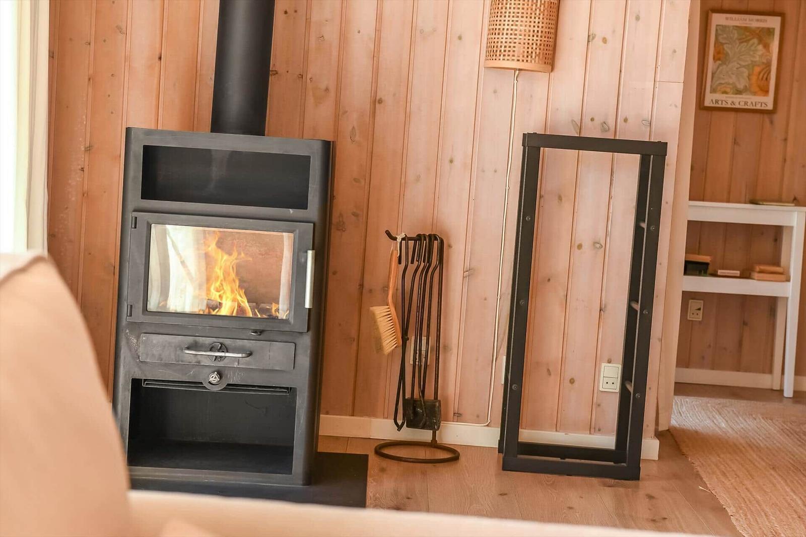 Holzwand mit Kaminofen, Feuer brennt, daneben steht ein schwarzer Metallrahmen.