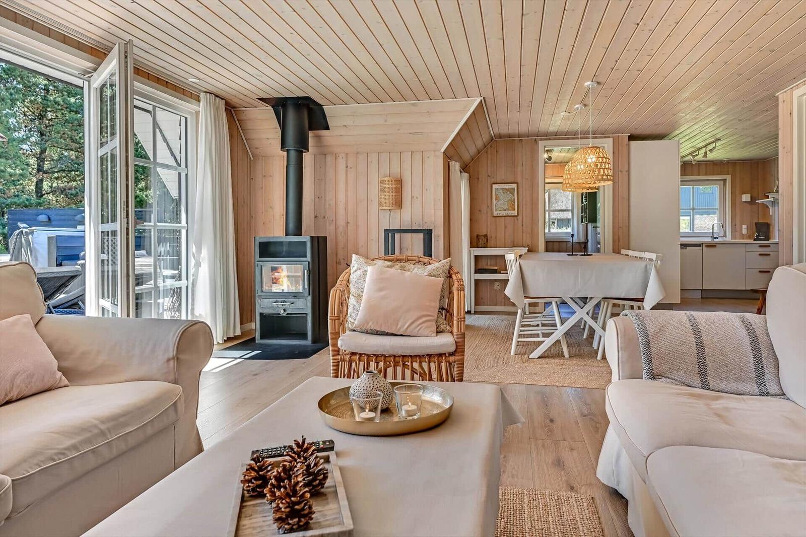 Wohnzimmer mit Kamin, Esstisch und Küche im Hintergrund. Holzwände und -boden.